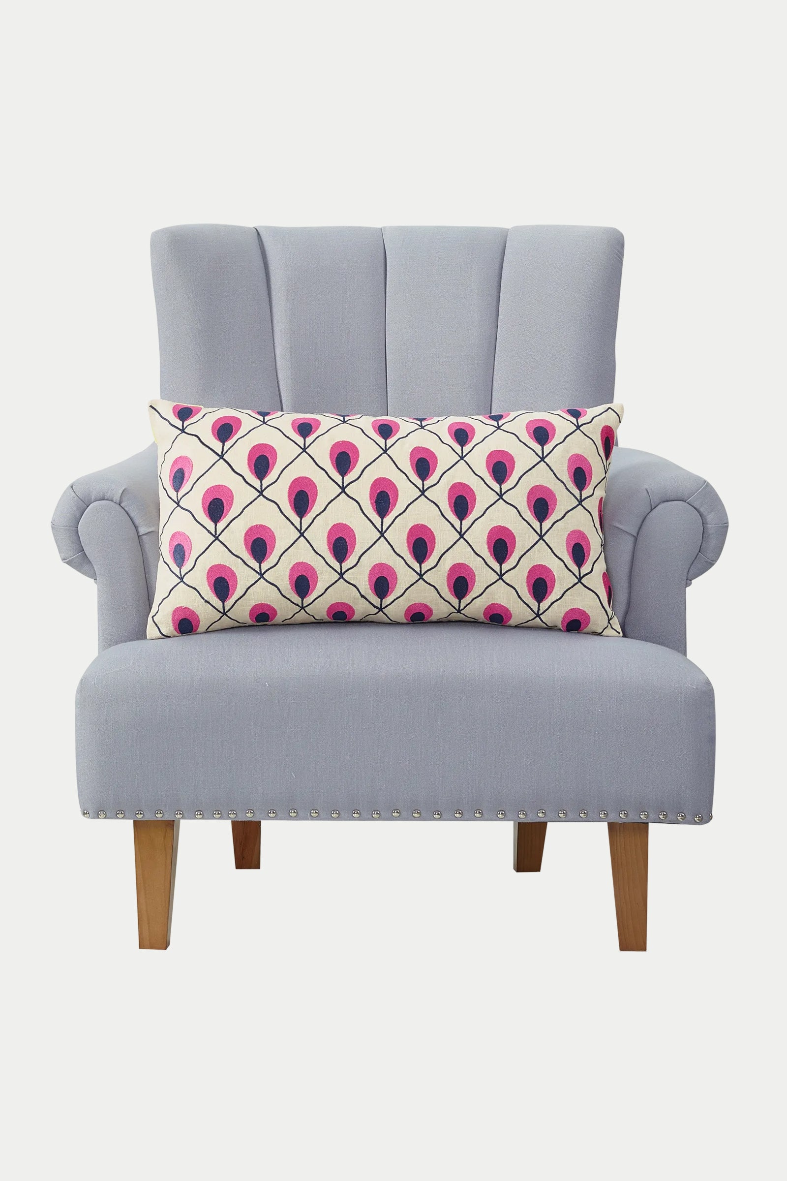 A light gray upholstered armchair with wooden legs, a high backrest, and silver nailhead trim, featuring the Roseville Embroidered Throw Pillow - Multi with a pink and purple geometric pattern.