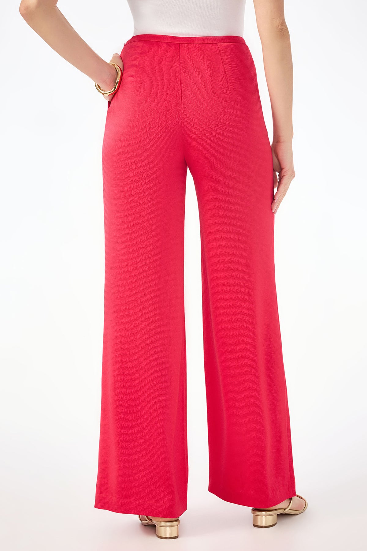 A person wearing the Tavia Wide-Leg Pant - Hammered Satin in bright red and a white top, shown from the back with one hand on their hip and gold sandals visible.