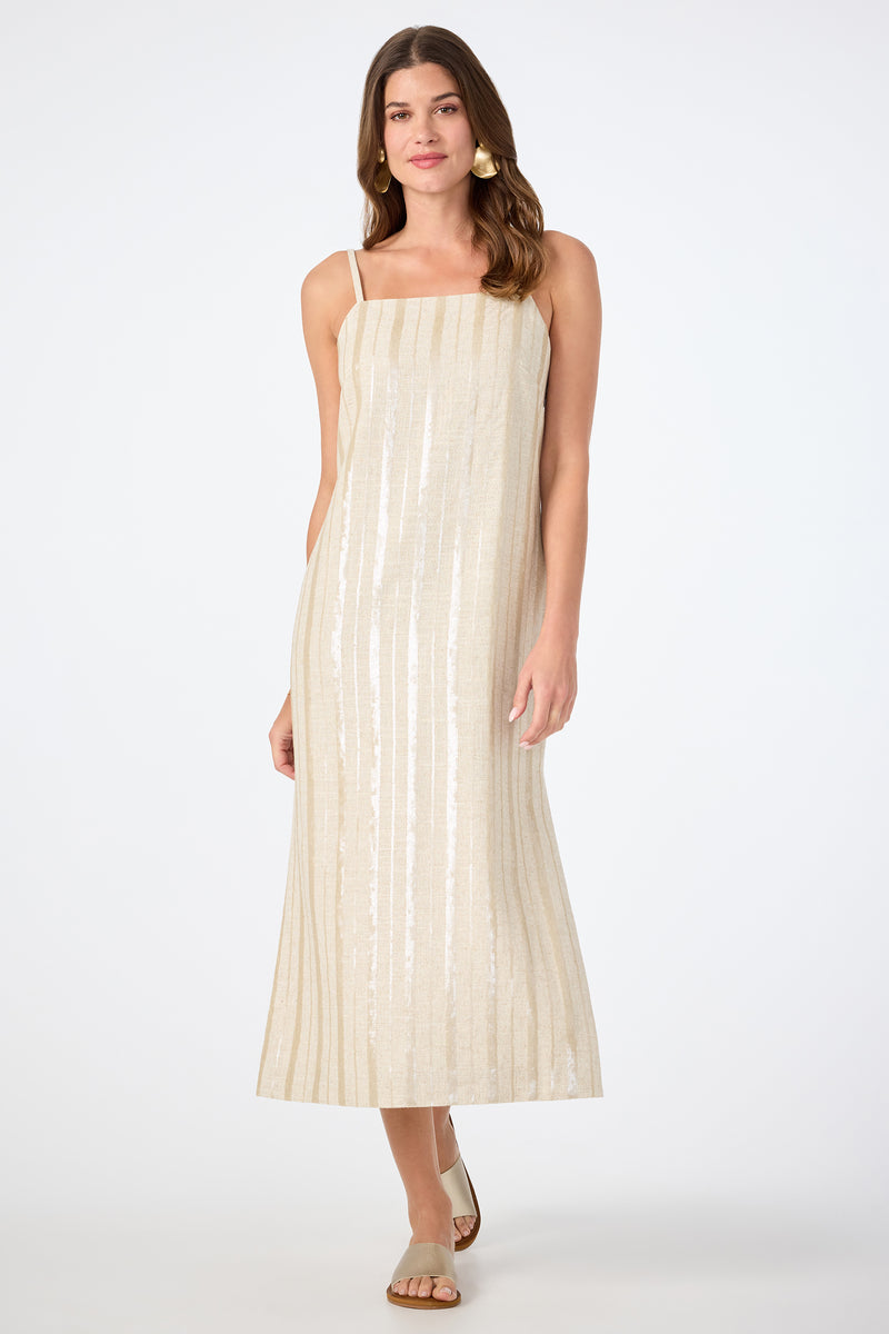 A woman stands against a plain white background wearing the Marita 3 Sleeveless Dress‚Äö√Ñ√Æan ankle-length, cream-colored dress with thin straps and subtle vertical stripes‚Äö√Ñ√Æpaired with flat sandals.