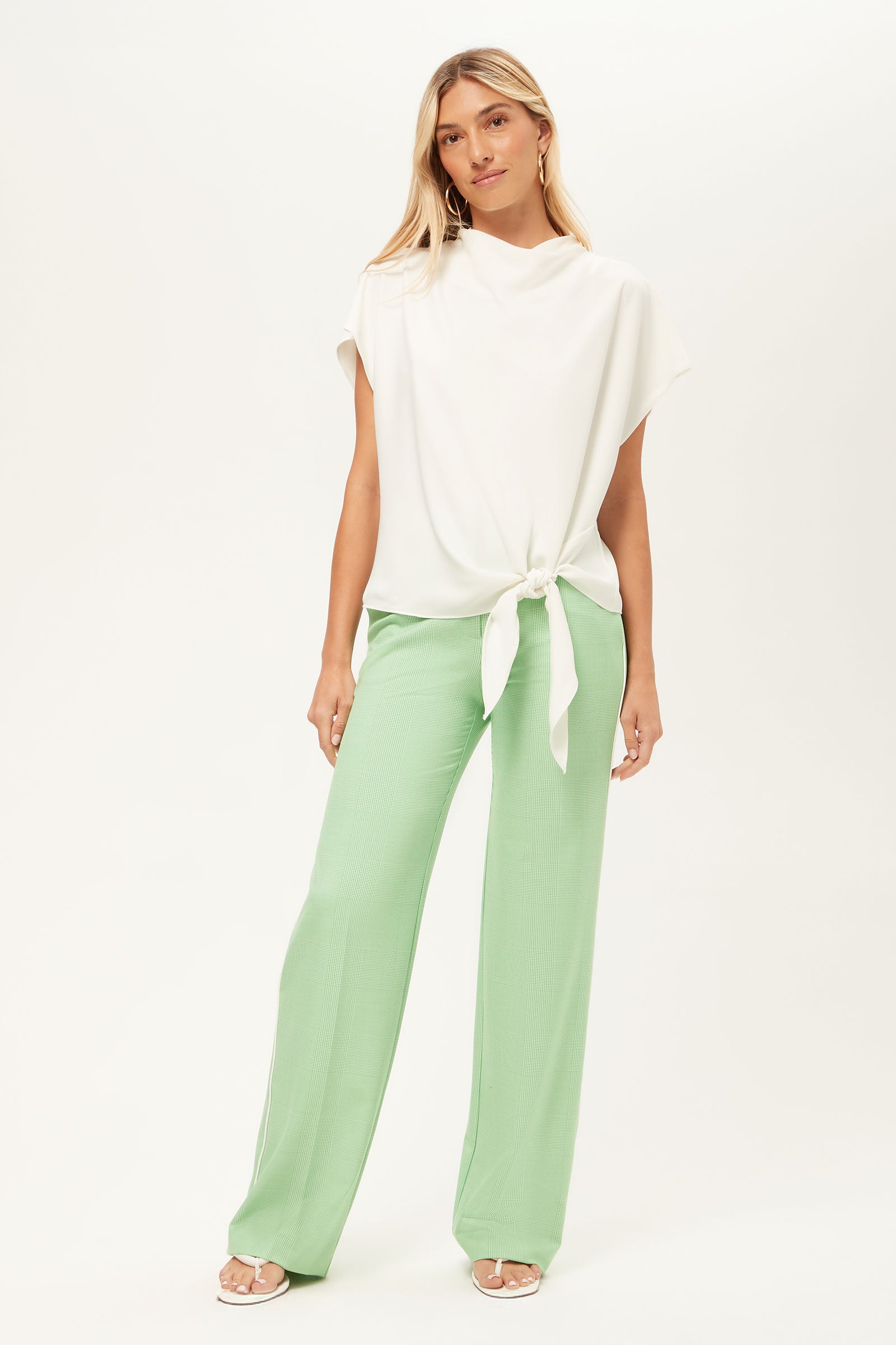 A woman with long blonde hair poses against a plain background wearing the Bisque Short-Sleeve Funnel Neck Top, styled loosely with neutral sandals and light green wide-leg pants for a relaxed look.
