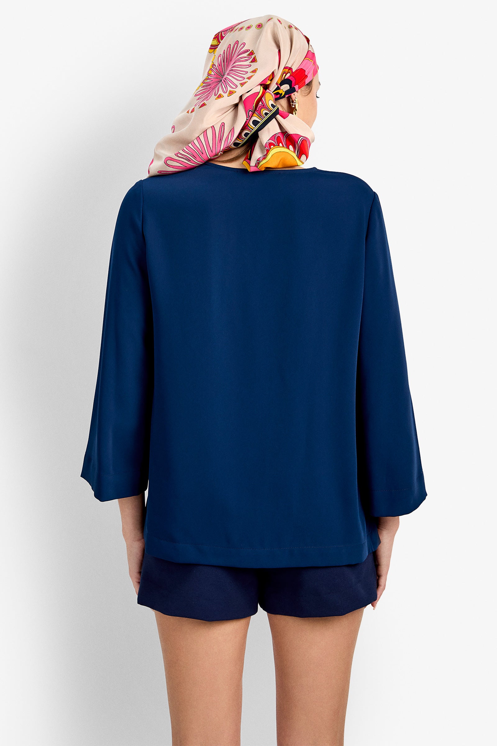 A person facing away from the camera wears a navy blue Catamaran Top, matching navy shorts, and a colorful scarf with pink and orange patterns covering their hair.