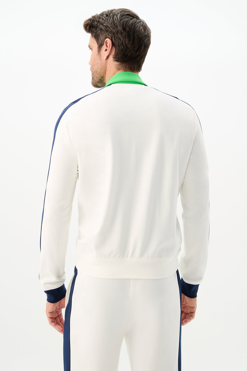 A man faces away from the camera, modeling the Ugo Track Jacket - Cozy Ponte, a white tracksuit featuring blue side stripes and a green collar against a simple light background.