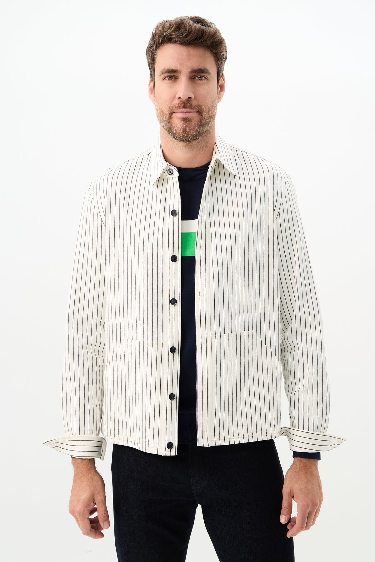 A man with short brown hair and a beard wears the Mulholland Shirt Jacket in Seles Stripe, color Whitewash/Ink, over a dark shirt and dark pants, standing against a plain white background.