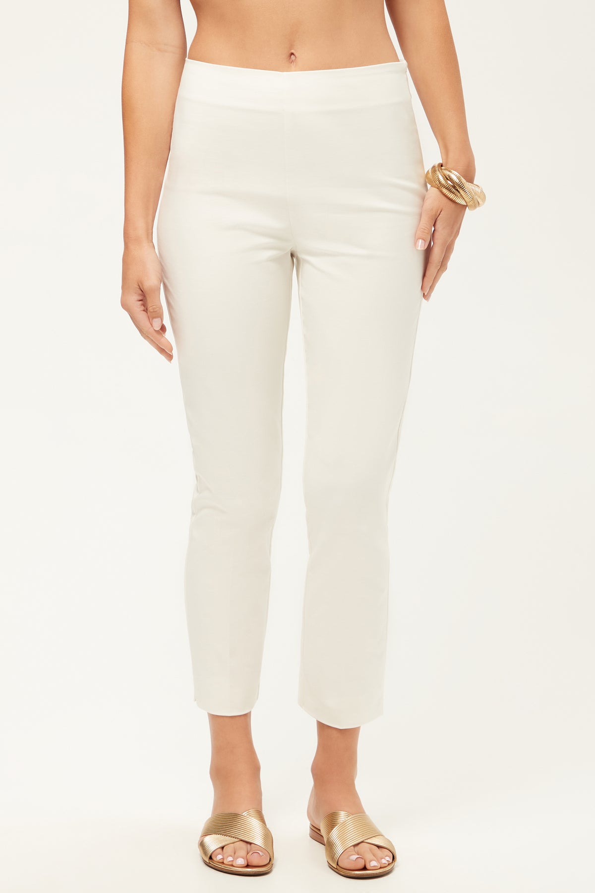 A person wearing Tie Breaker Slim Crop Pant in Whitewash, gold slide sandals, and a chunky gold bracelet stands against a plain light background.