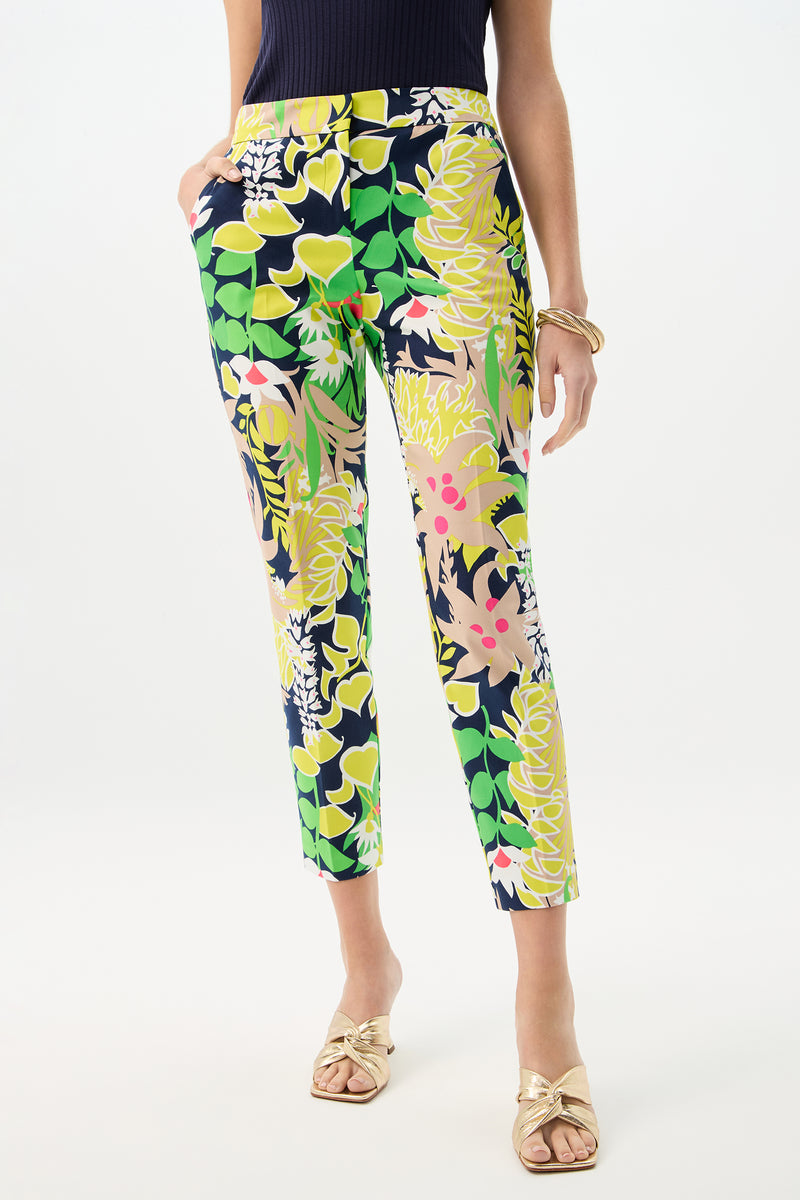 A woman wears the Aubree 2 Pant - PS Eternal in Palm Springs Eternal, featuring vibrant florals, paired with a sleeveless black top, gold sandals, and gold bangles, with one hand in her pocket.