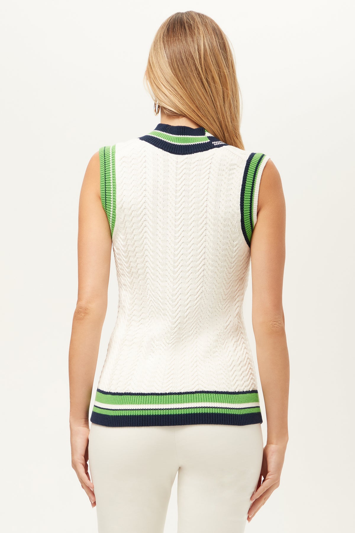A woman with long, blonde hair is shown from the back, wearing the Seapointe 2 Sleeveless Knit Vest—a white sweater vest with green and navy stripes—paired with white pants.