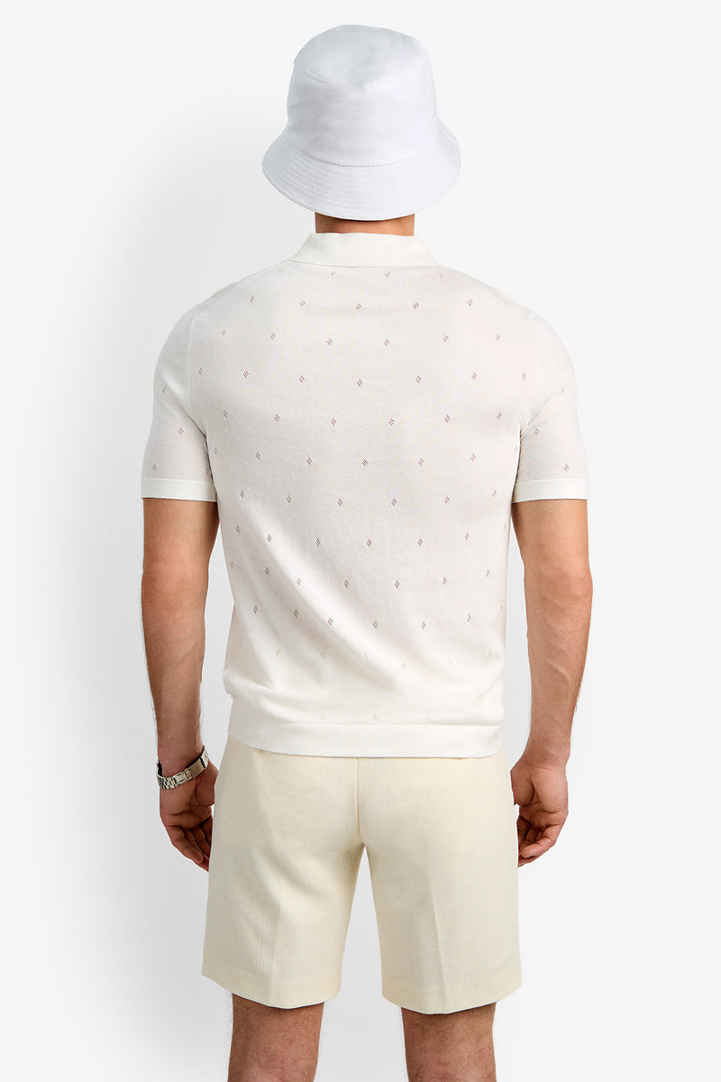 A person faces away, wearing a white bucket hat, the Nicholas Short-Sleeve Polo with a subtle pattern, light beige shorts, and a watch on their left wrist against a plain background.