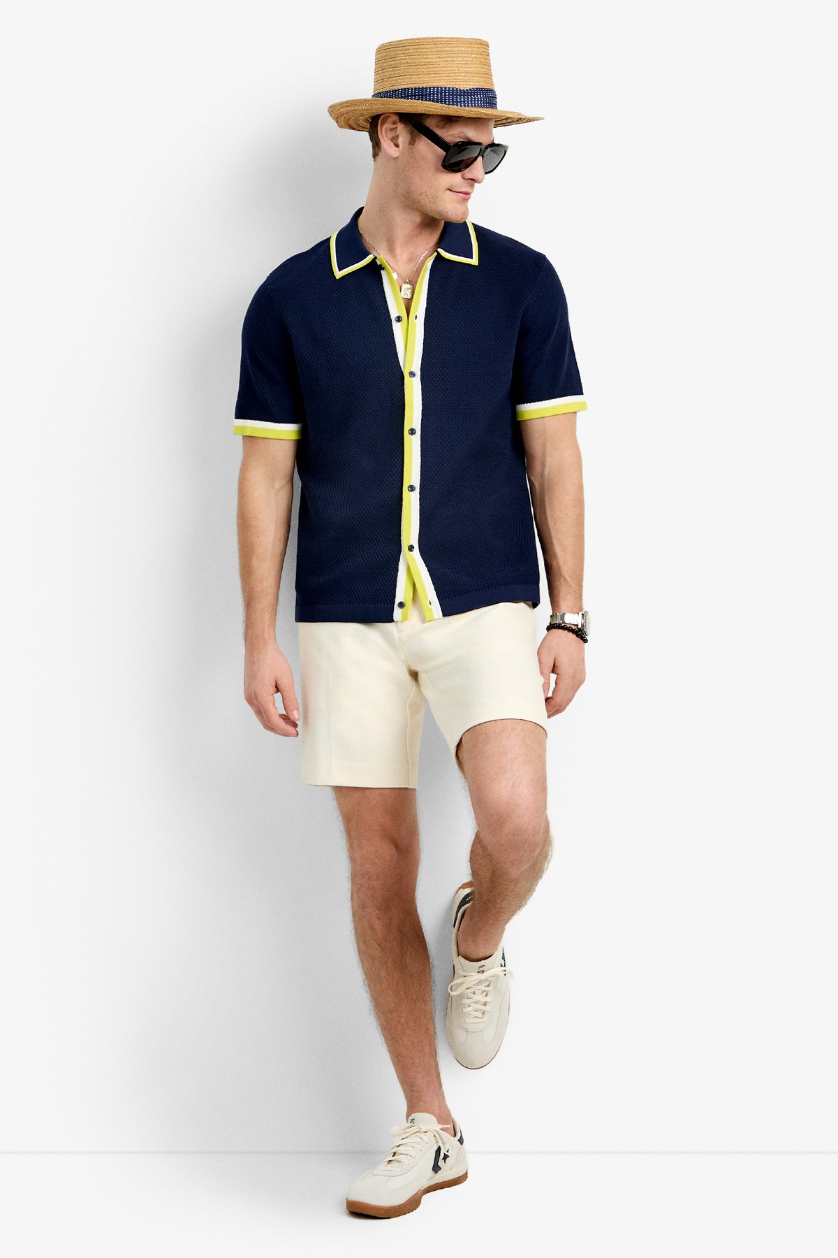 A man in the Kylian Short-Sleeve Polo, cream shorts, white sneakers, a straw hat, and sunglasses stands against a plain backdrop, looking to the side and smiling.