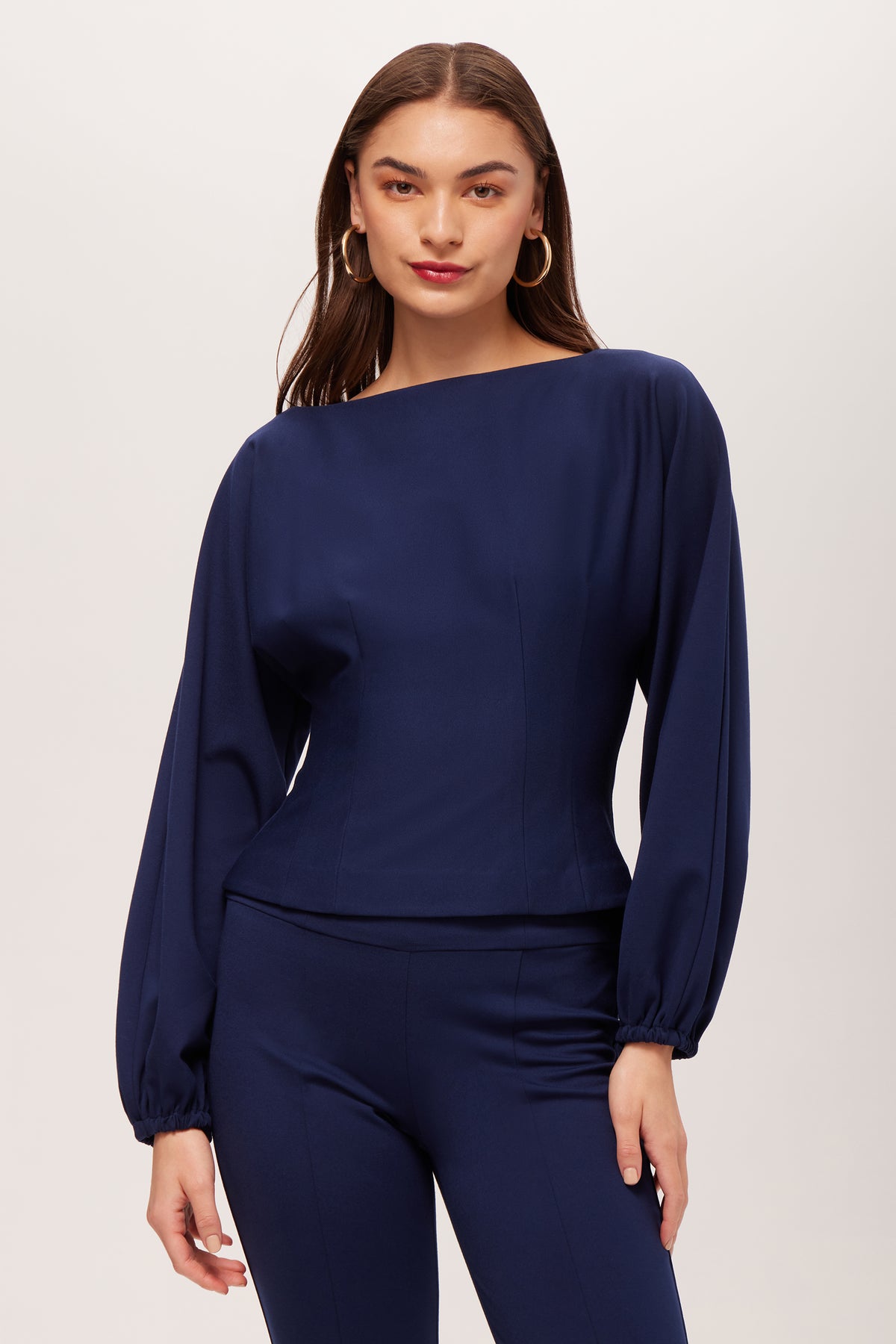 A woman wears the Prime Long-Sleeve Boatneck Top in Ink with matching blue pants, standing against a plain light background.