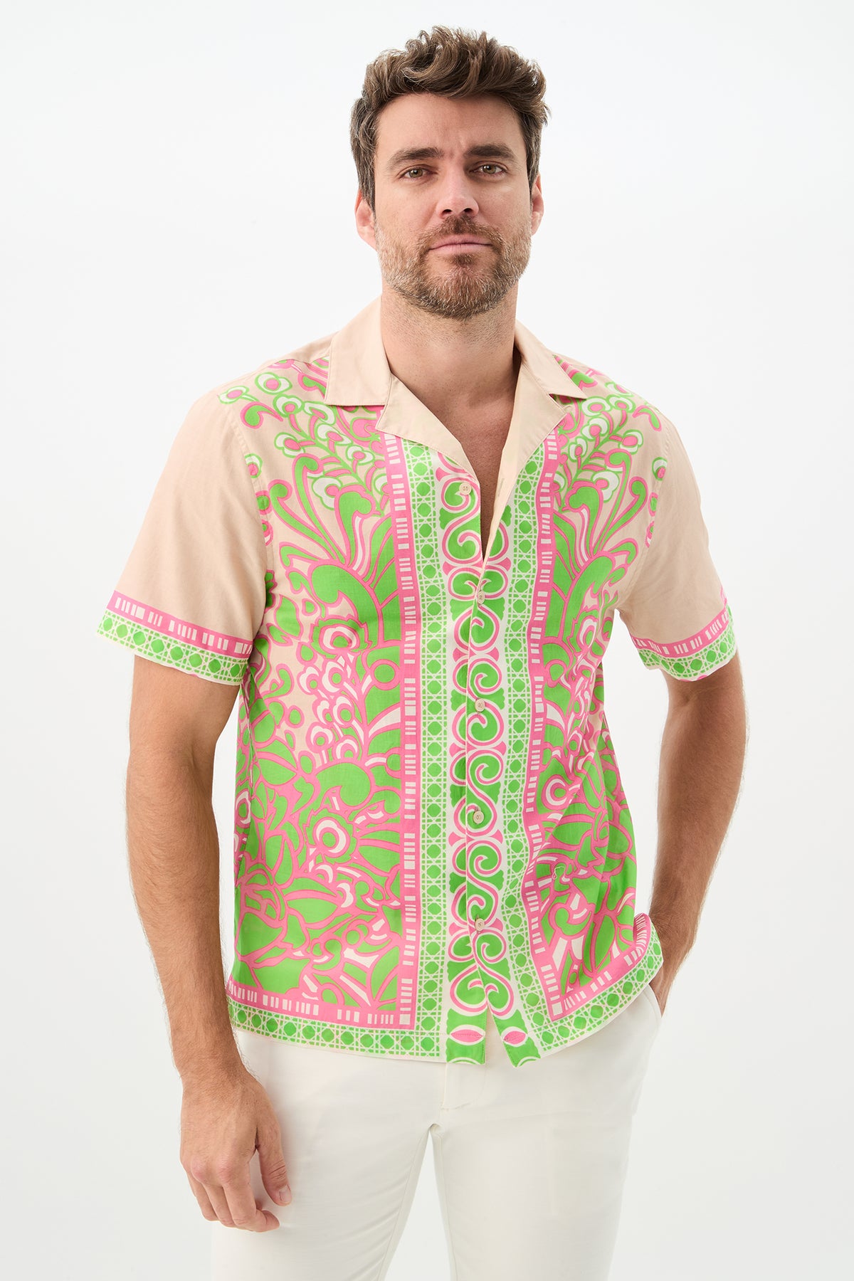 A man with short brown hair and a beard wears the Josue Short-Sleeve Shirt in Petra Floral, paired with white pants, standing against a plain white background.