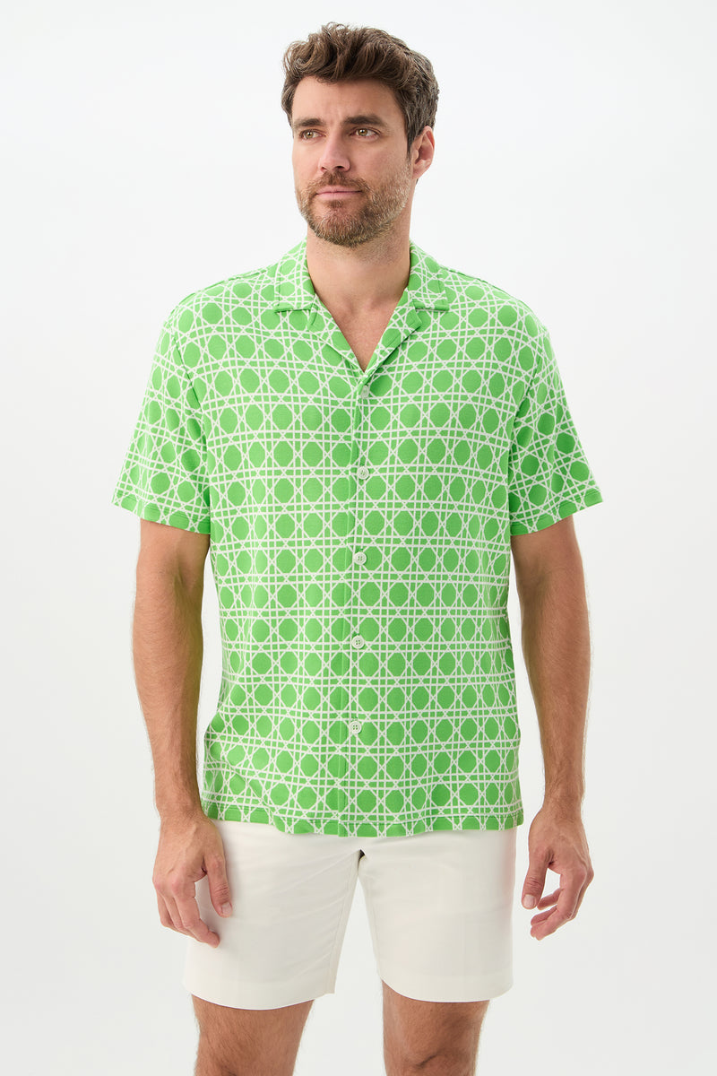 A man with short brown hair and a beard wears the Felix Short-Sleeve Knit Shirt in Billie Jean, paired with white shorts, standing against a plain white background.