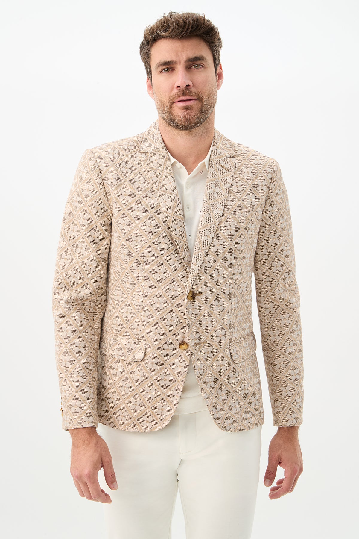 A man with short brown hair and a beard wears the Thurston Blazer in Beach Metallic Daisy Jacquard over a white shirt and white pants, standing against a plain white background.