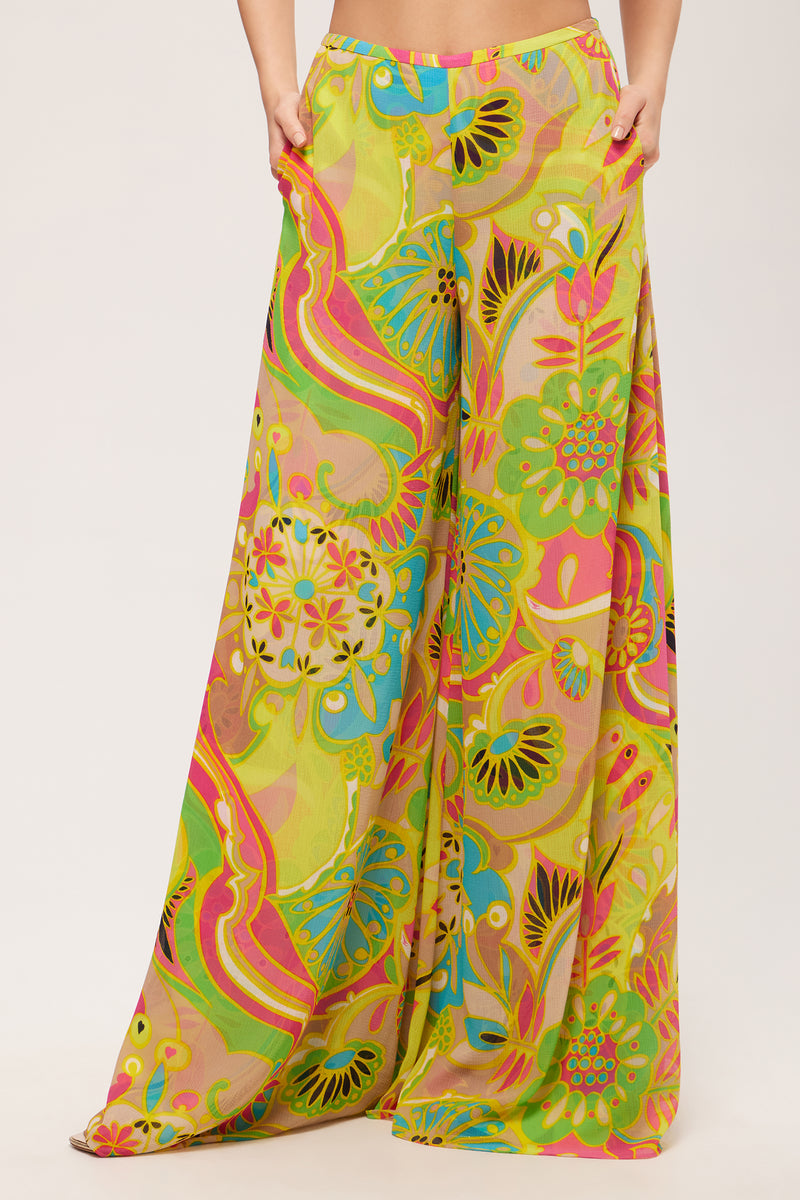 Woman wears the Jack Wide-Leg Pant in Venus, featuring a flowy, high-waisted fit and a vibrant multicolored abstract floral pattern in shades of green, yellow, pink, and orange against a plain background.