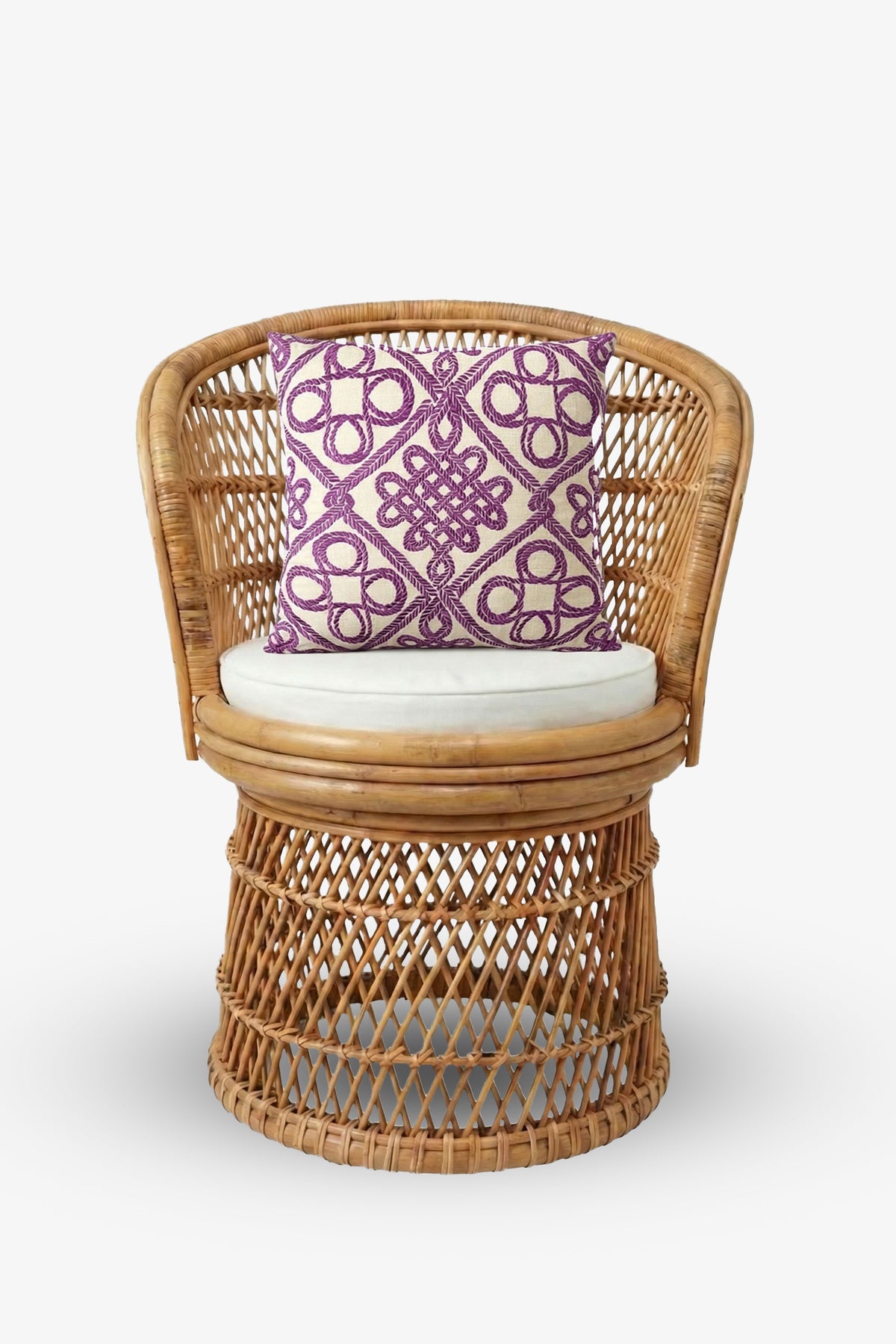 A round rattan chair with a beige seat cushion is accented by the Embroidered Square Pillow, featuring a purple geometric pattern, all set against a plain white background.