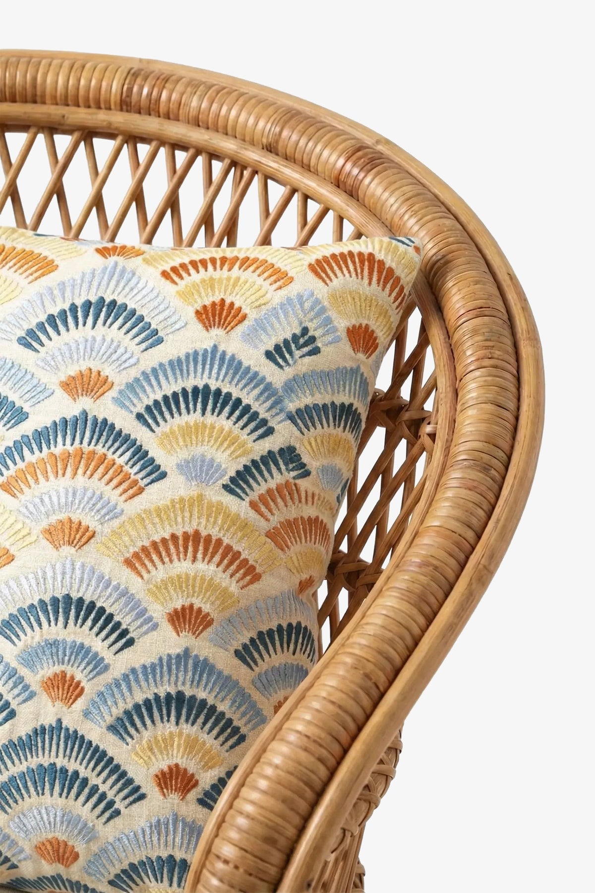 A close-up of a wicker chair adorned with the Pasadena Embroidered Square Pillow, which features a decorative fan-patterned design in blue, orange, yellow, and gray tones.