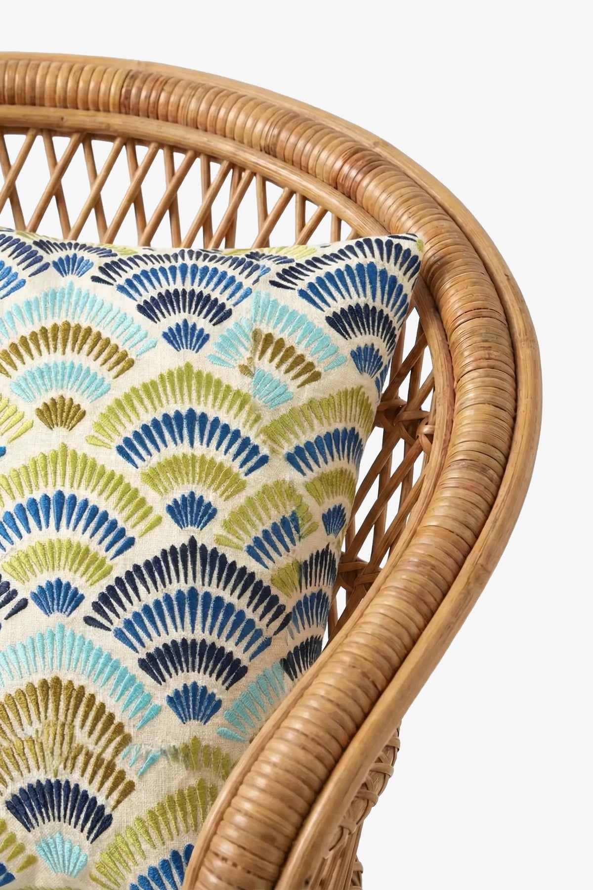 A close-up of a wicker chair with the Pasadena Embroidered Square Pillow, which features blue, green, and teal fan-shaped patterns on a white background.