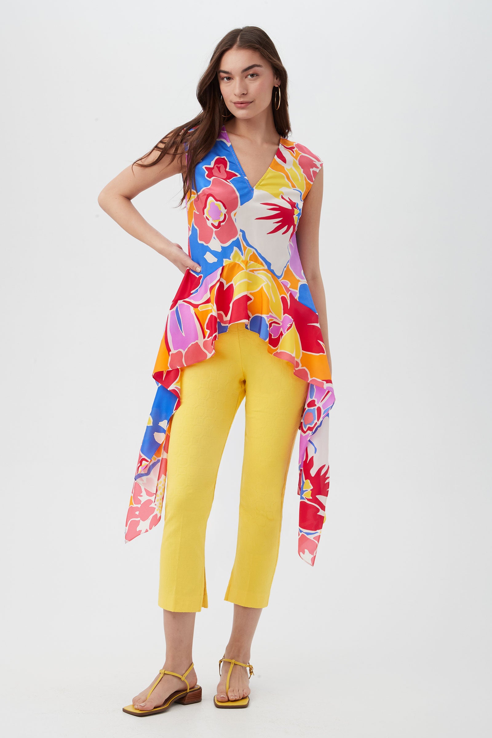 A woman stands confidently in a colorful sleeveless floral top with an asymmetric hem, paired with Pop Slim-Leg Stretch Pants in bright yellow and yellow sandals, posing against a plain white background.