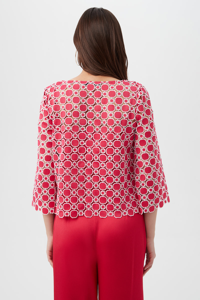 A woman with long brown hair, seen from the back, wears the Sun Top—a red and white geometric-patterned, semi-sheer top with three-quarter sleeves—paired with bright red pants against a plain white background.