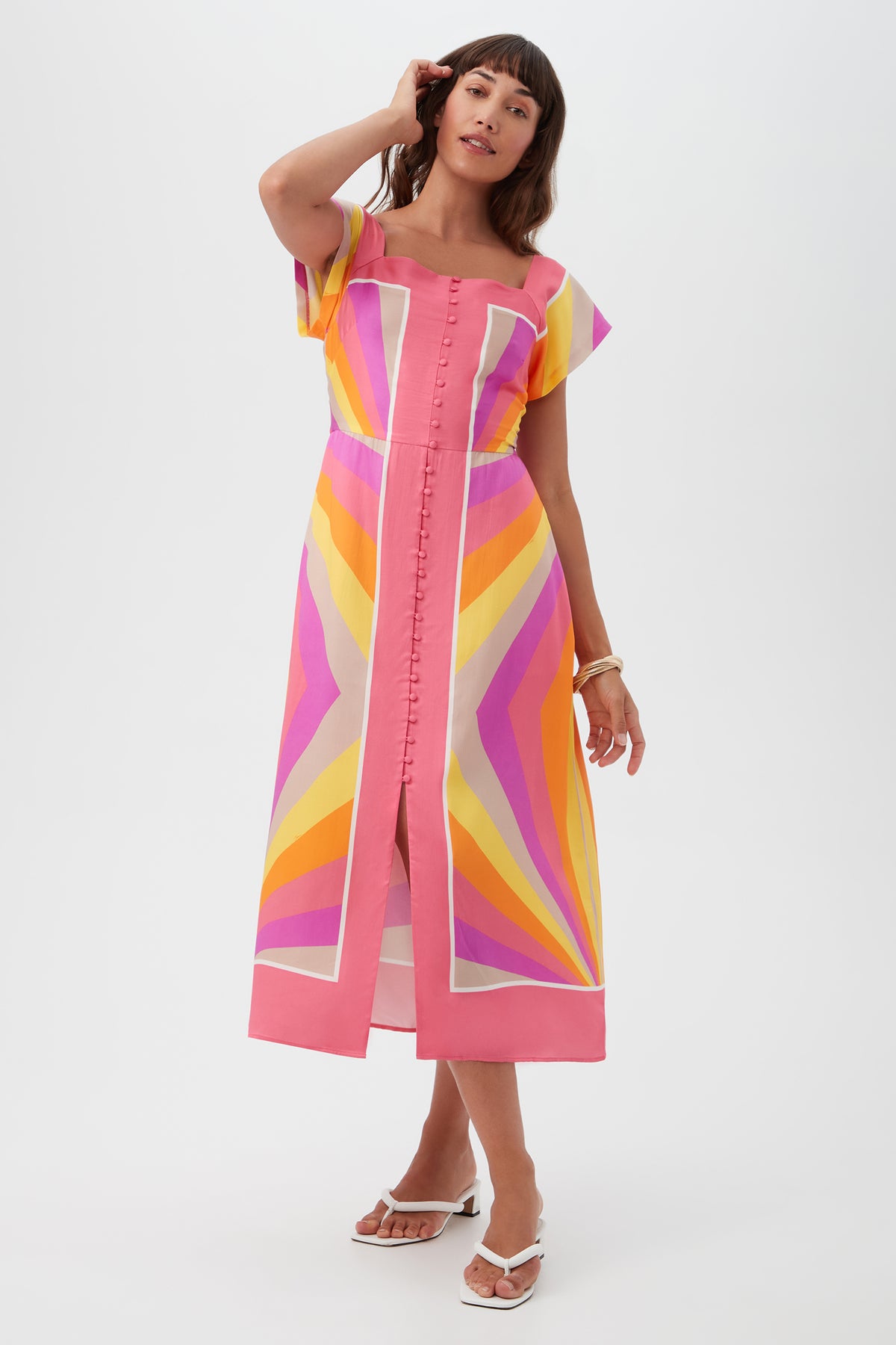 A woman in the Après Short-Sleeve Dress, a multi-colored geometric midi with short sleeves and a front slit, stands against a white background.