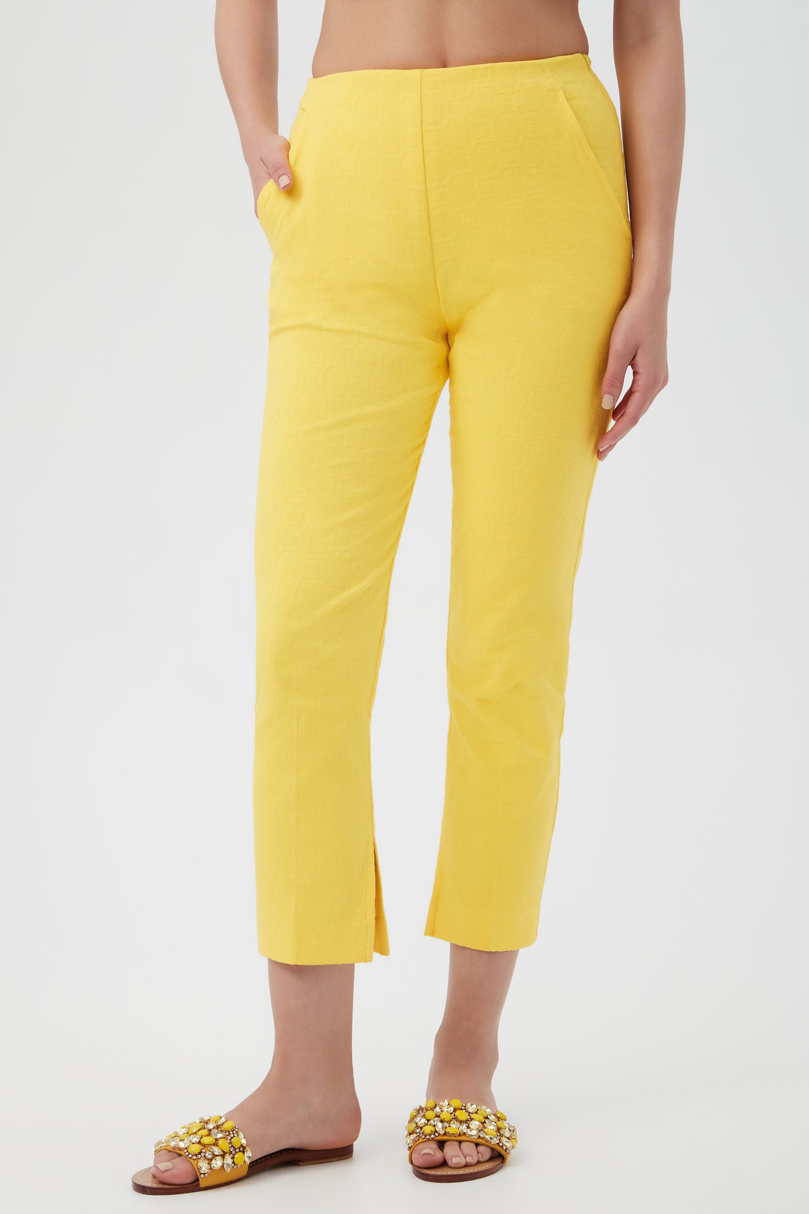 Someone wearing Pop Slim-Leg Stretch Pants in Lavandou Lemon, featuring ankle-length style and side pockets, paired with flat sandals adorned with yellow and white beads, stands against a plain white background.