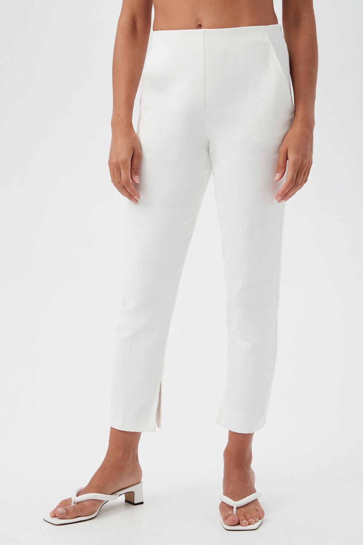 A person wears the Pop Slim-Leg Stretch Pants—high-waisted, white, textured ankle-length with small front slits—paired with white open-toe sandals against a plain white background.