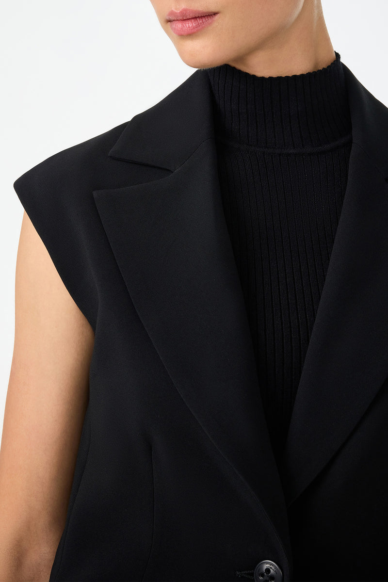 A person models the Boabab Sleeveless Jacket over a ribbed black turtleneck, shown from shoulders to chin against a plain light background.