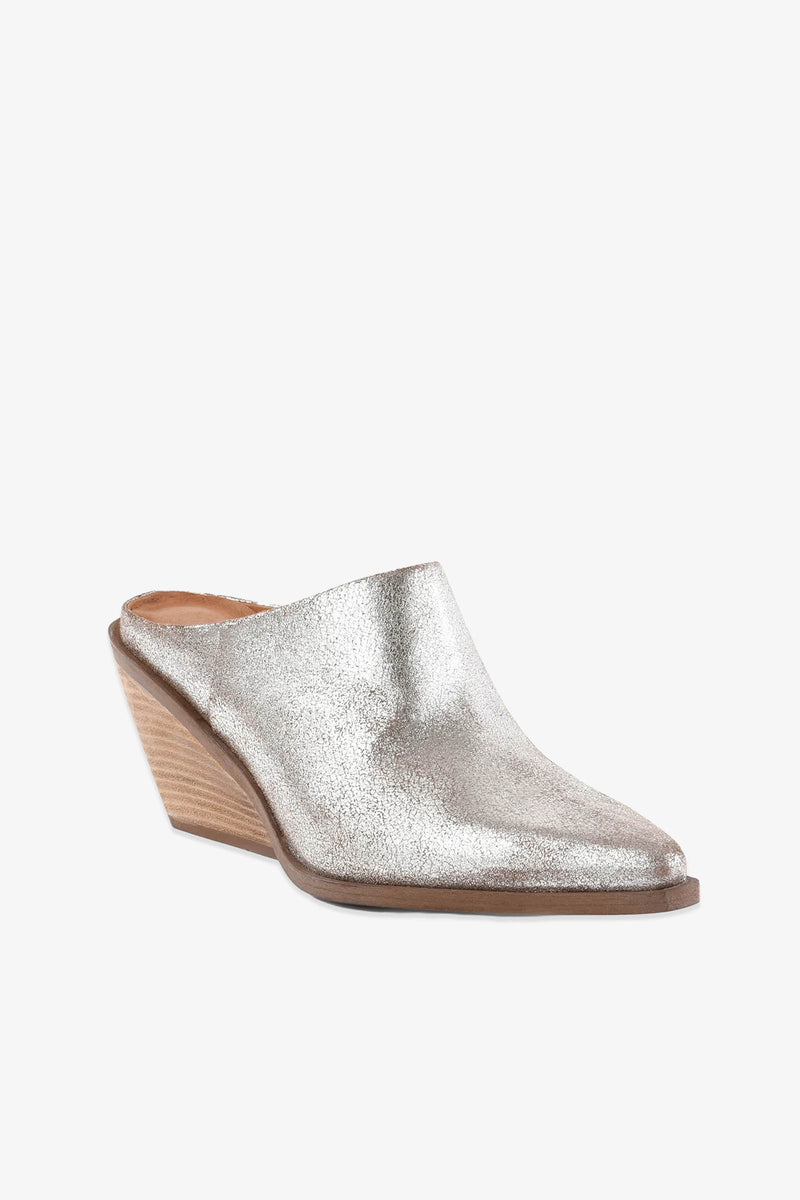 The Morning Joe Mule is a silver metallic mule featuring a pointed toe and a low, angled wooden wedge heel, displayed on a white background.