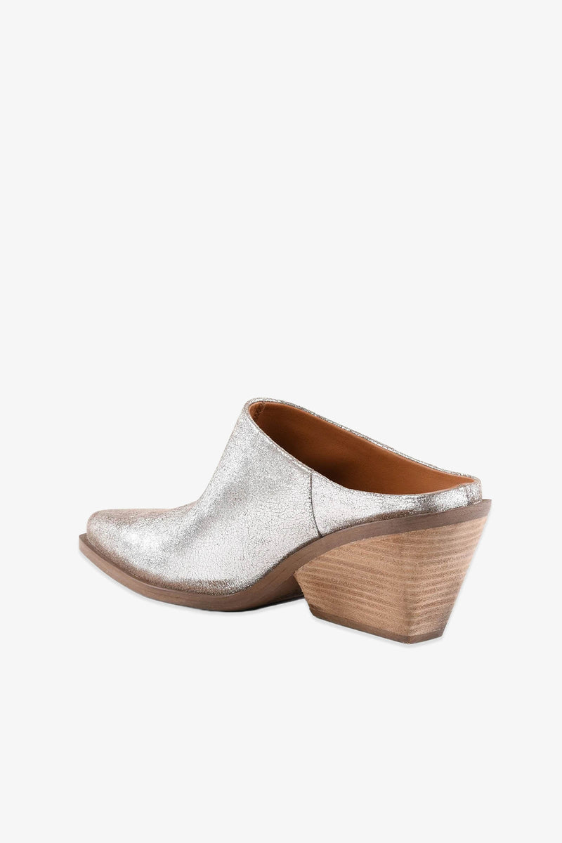 The Morning Joe Mule is a silver slip-on mule featuring a pointed toe and a chunky, angled wooden heel, displayed in profile against a white background.