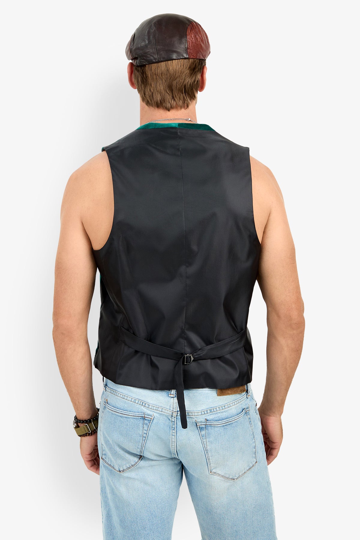 A man is seen from the back wearing the Irving Velvet Vest, blue jeans, and a brown leather cap against a plain white background.