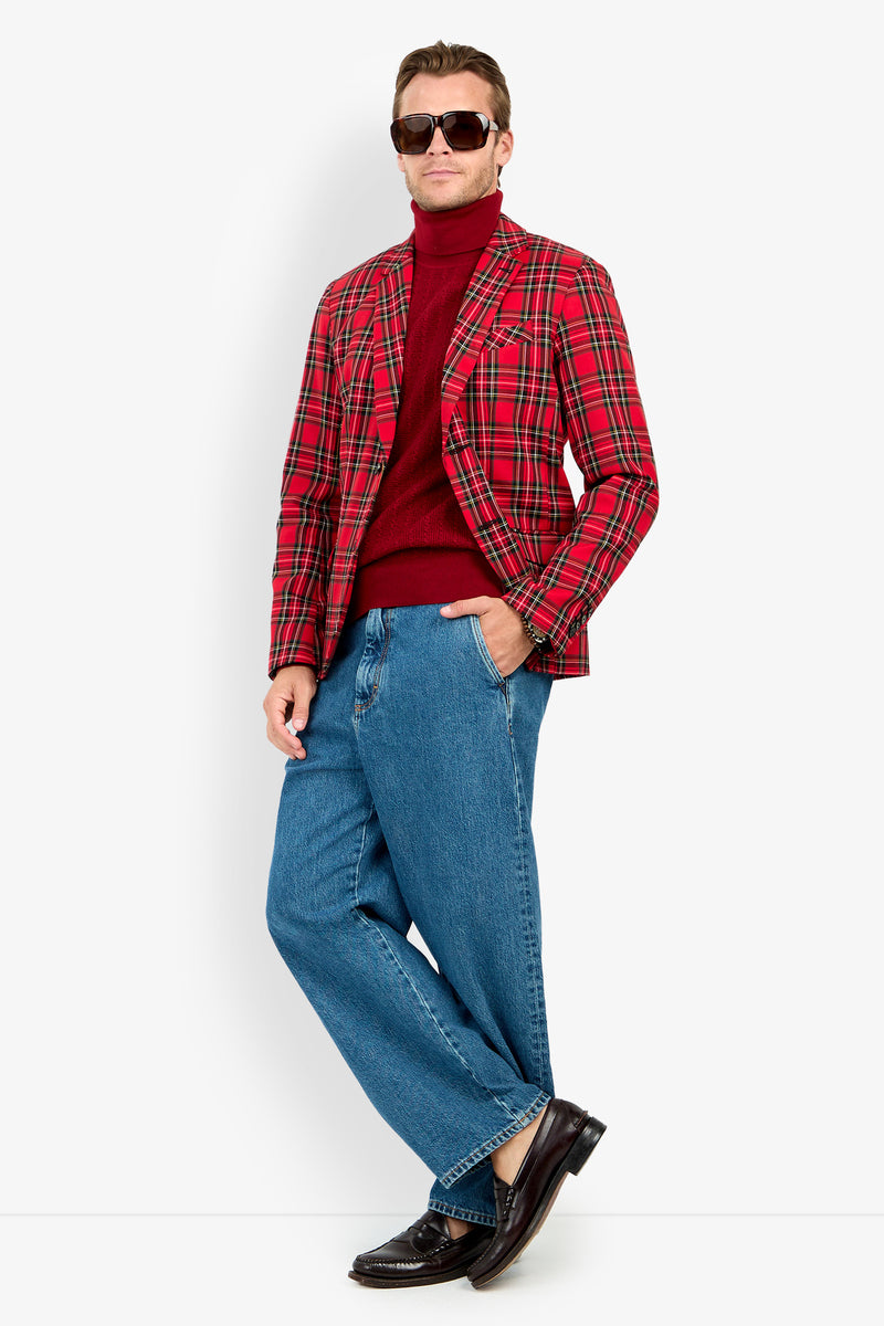 A person wearing sunglasses, the Thurston Blazer, a red turtleneck sweater, blue wide-leg jeans, and dark loafers stands against a plain white background.