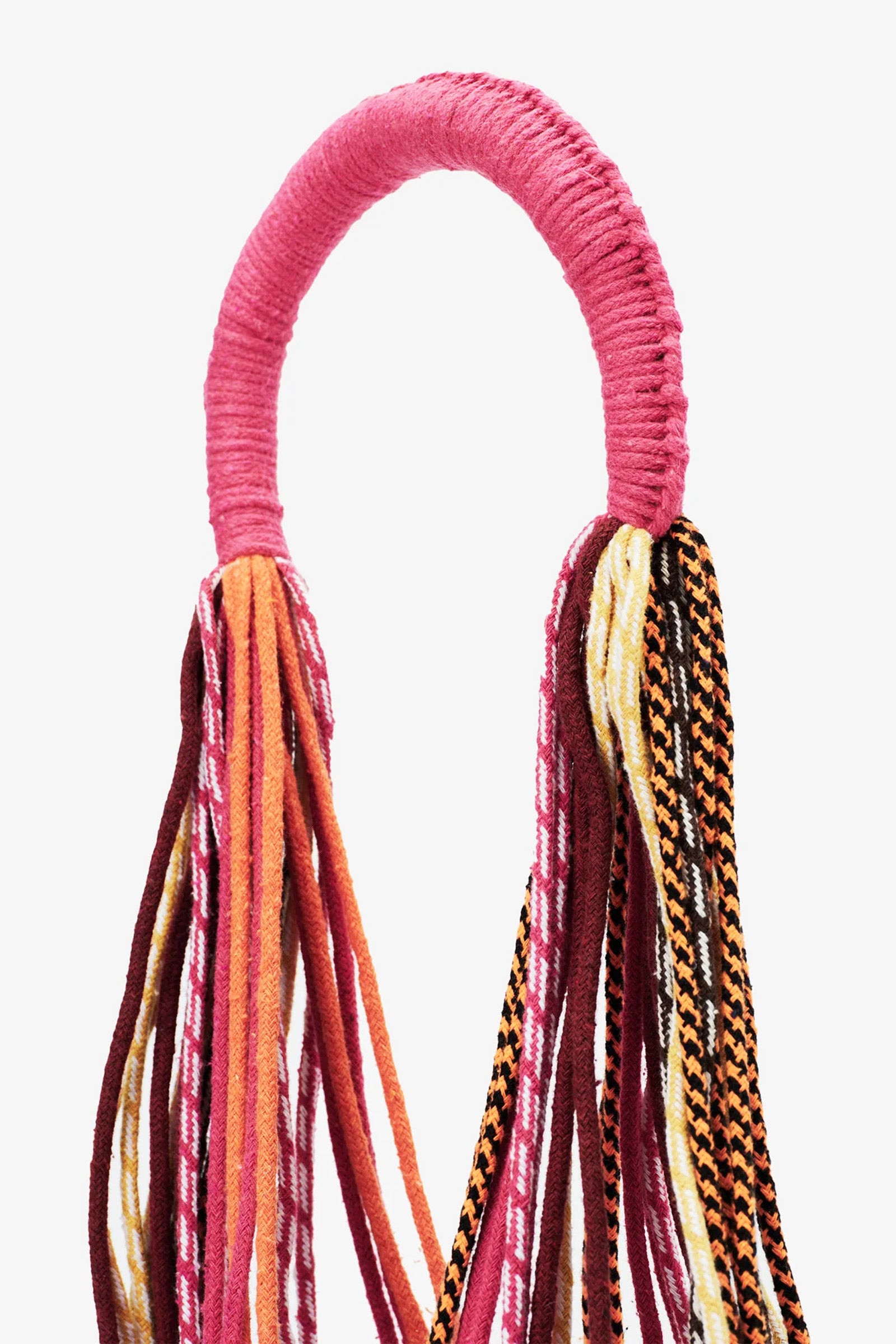 The Nannacay Kim Woven Bag features a pink fabric-wrapped handle with multiple long, colorful woven textile strands hanging down, showcasing patterns in red, pink, orange, white, and black.