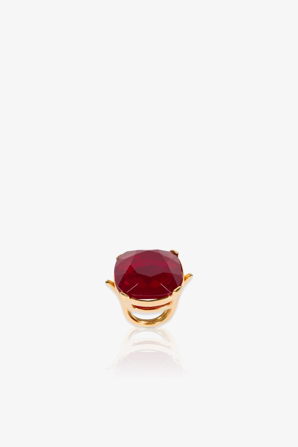 A Ruby Faceted Cocktail Ring featuring a large, faceted deep red gemstone set in a prong setting is displayed on a white background with a subtle reflection beneath it.