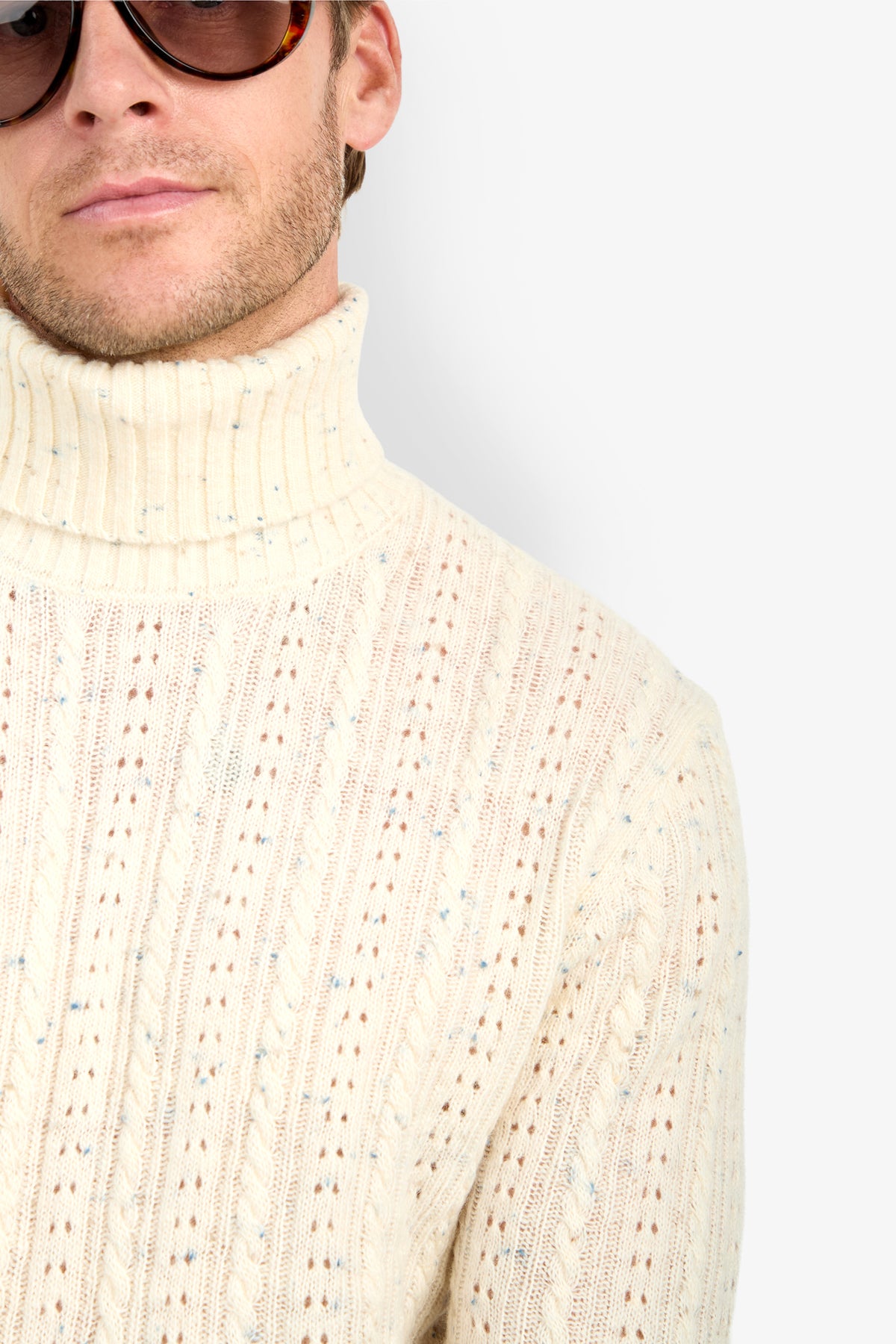 A person in dark sunglasses and a cream-colored Wesley Turtleneck Sweater, shown from the shoulders up against a plain white background.