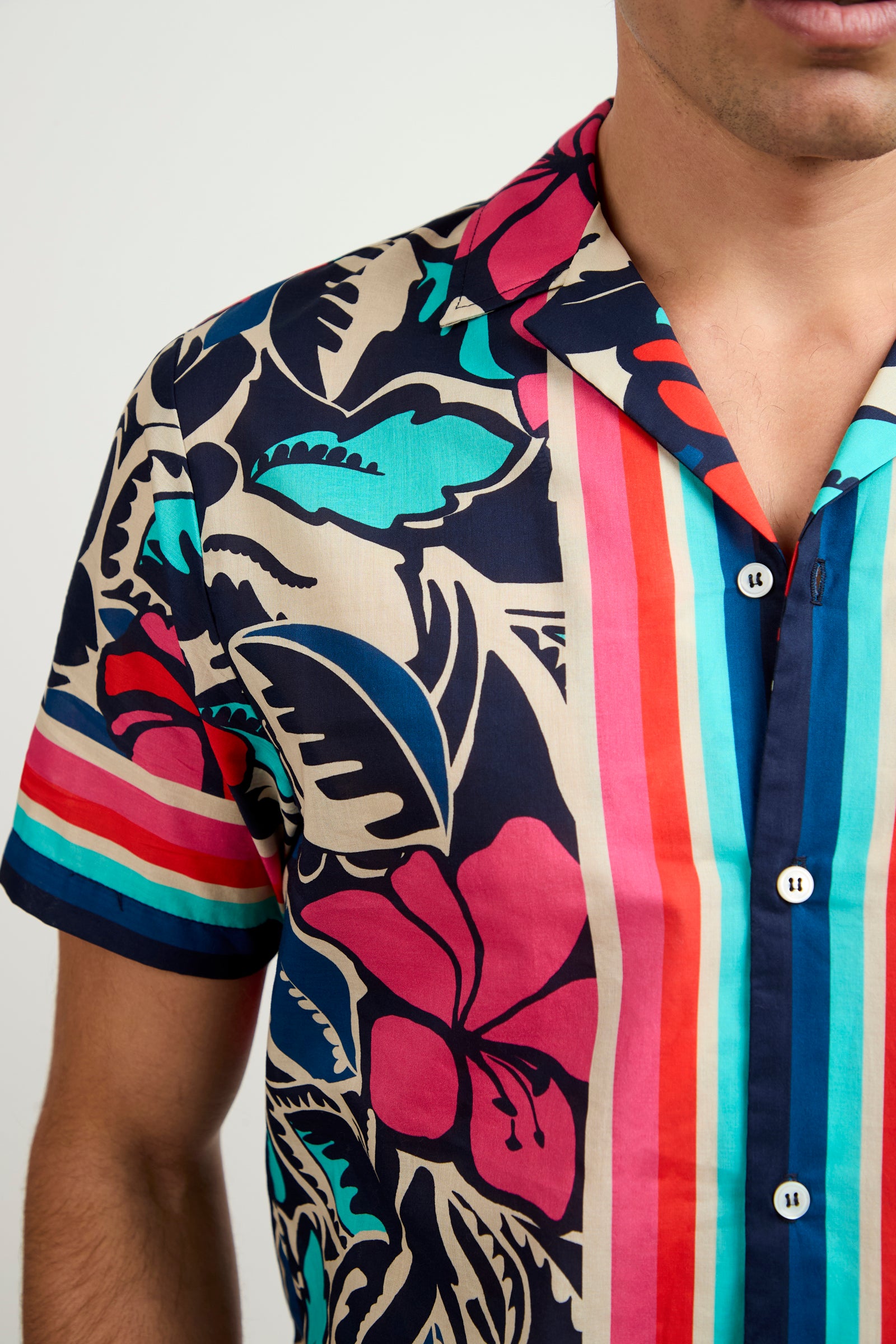 A person wearing the Josue Short-Sleeve Shirt - Copacabana, featuring bold blue, red, pink, and beige floral and striped patterns, shown from shoulders to mid-torso.