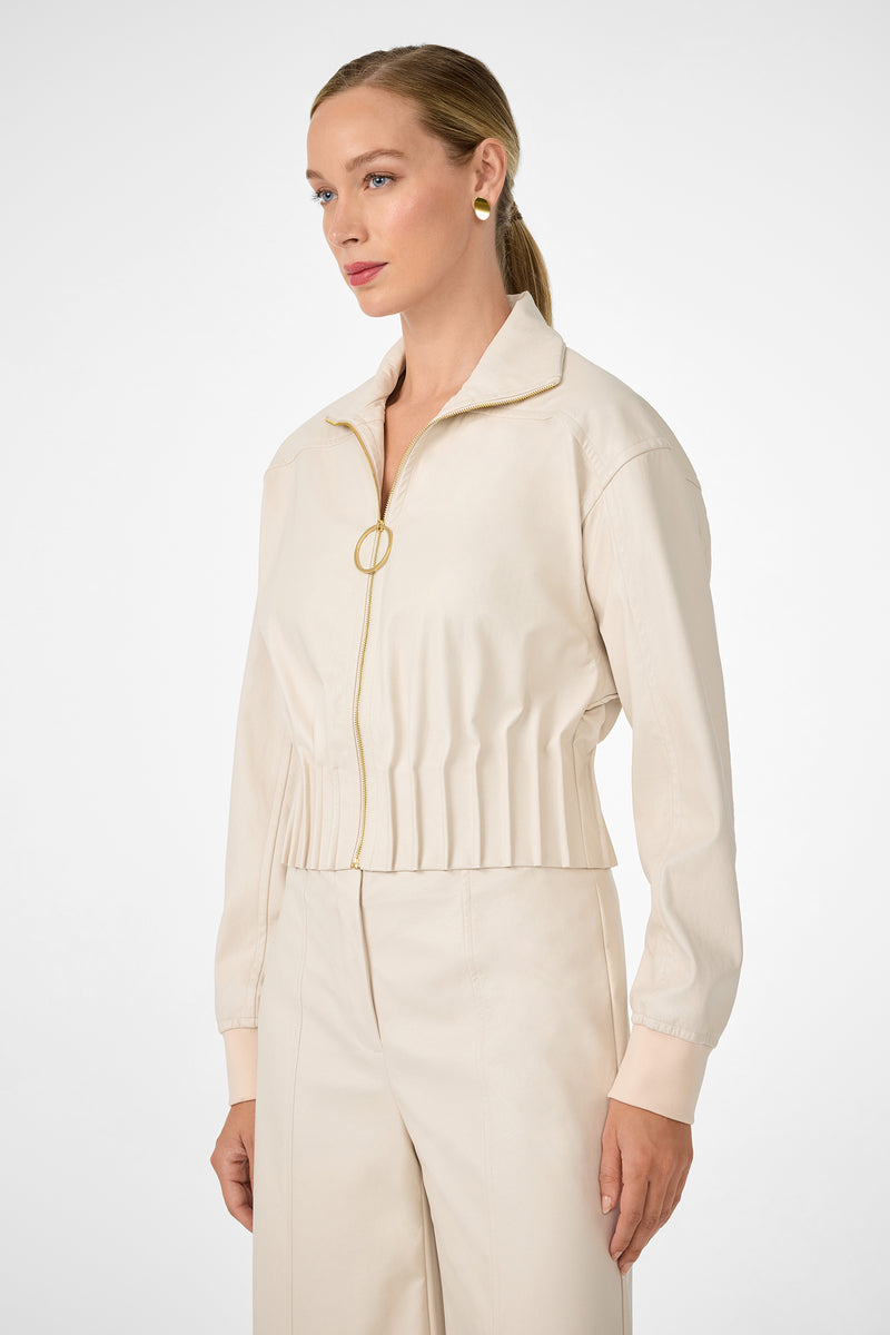 A woman with blonde hair in a low ponytail wears the cream Outrun Jacket with matching high-waisted pants, standing against a plain white background and looking to the side.