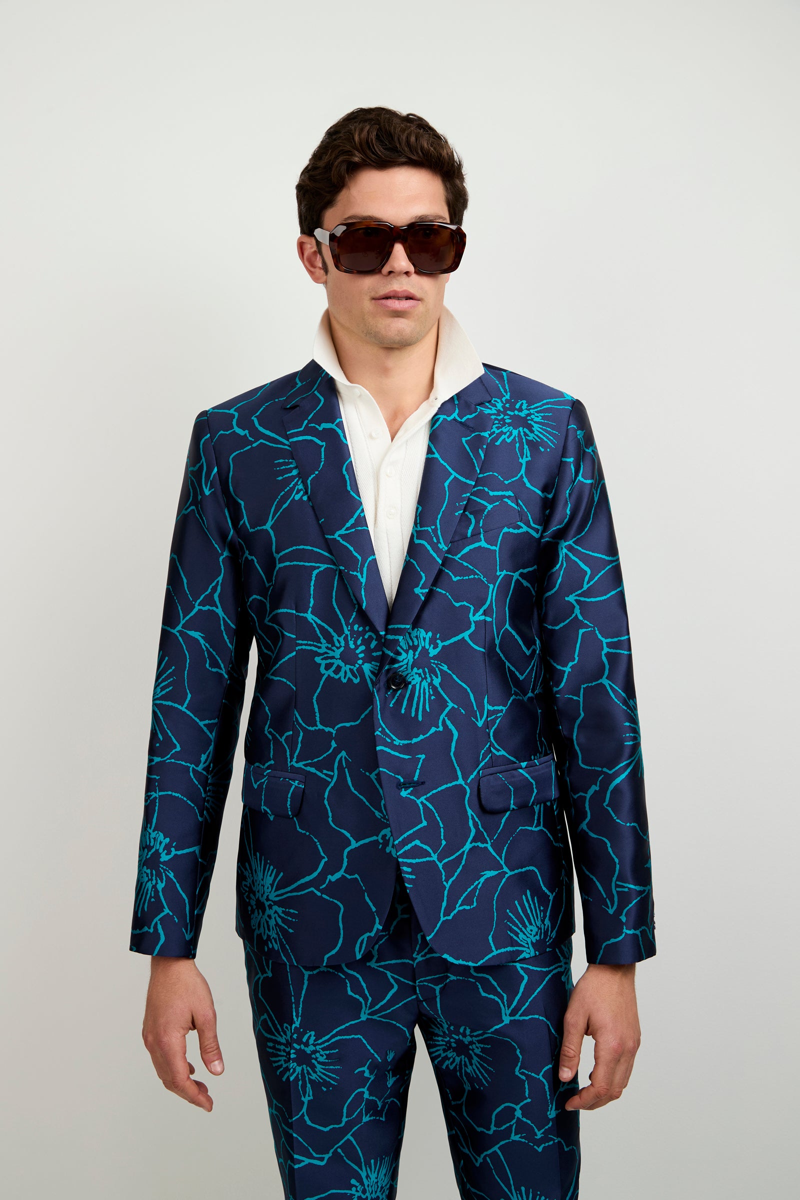 A man in dark sunglasses, a white collared shirt, and the Thurston Blazer in Jucara Jacquard stands against a plain light-colored background.