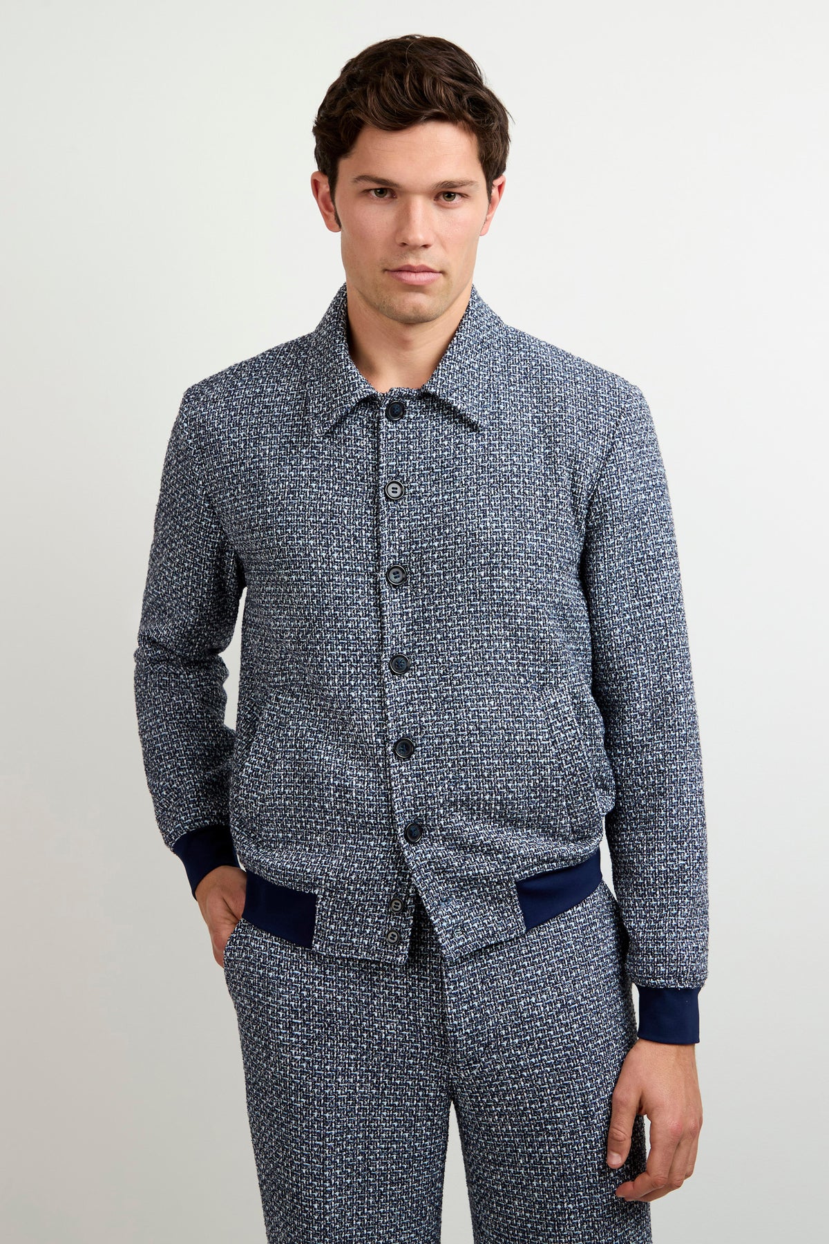 A man wears the Lowen Tweed Jacket in Selva Suiting with matching pants, standing against a plain light background, one hand in his pocket and a neutral expression.
