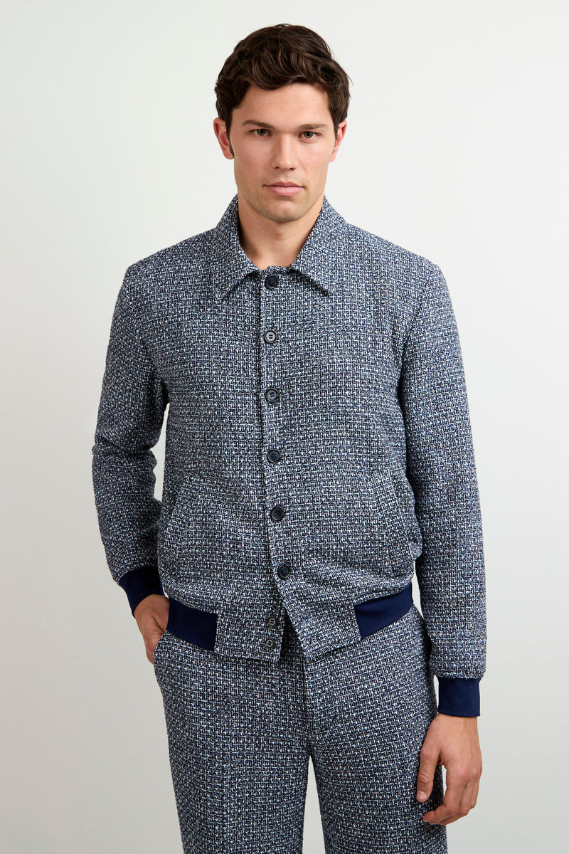 A man wears the Lowen Tweed Jacket in Selva Suiting with matching pants, standing against a plain light background, one hand in his pocket and a neutral expression.