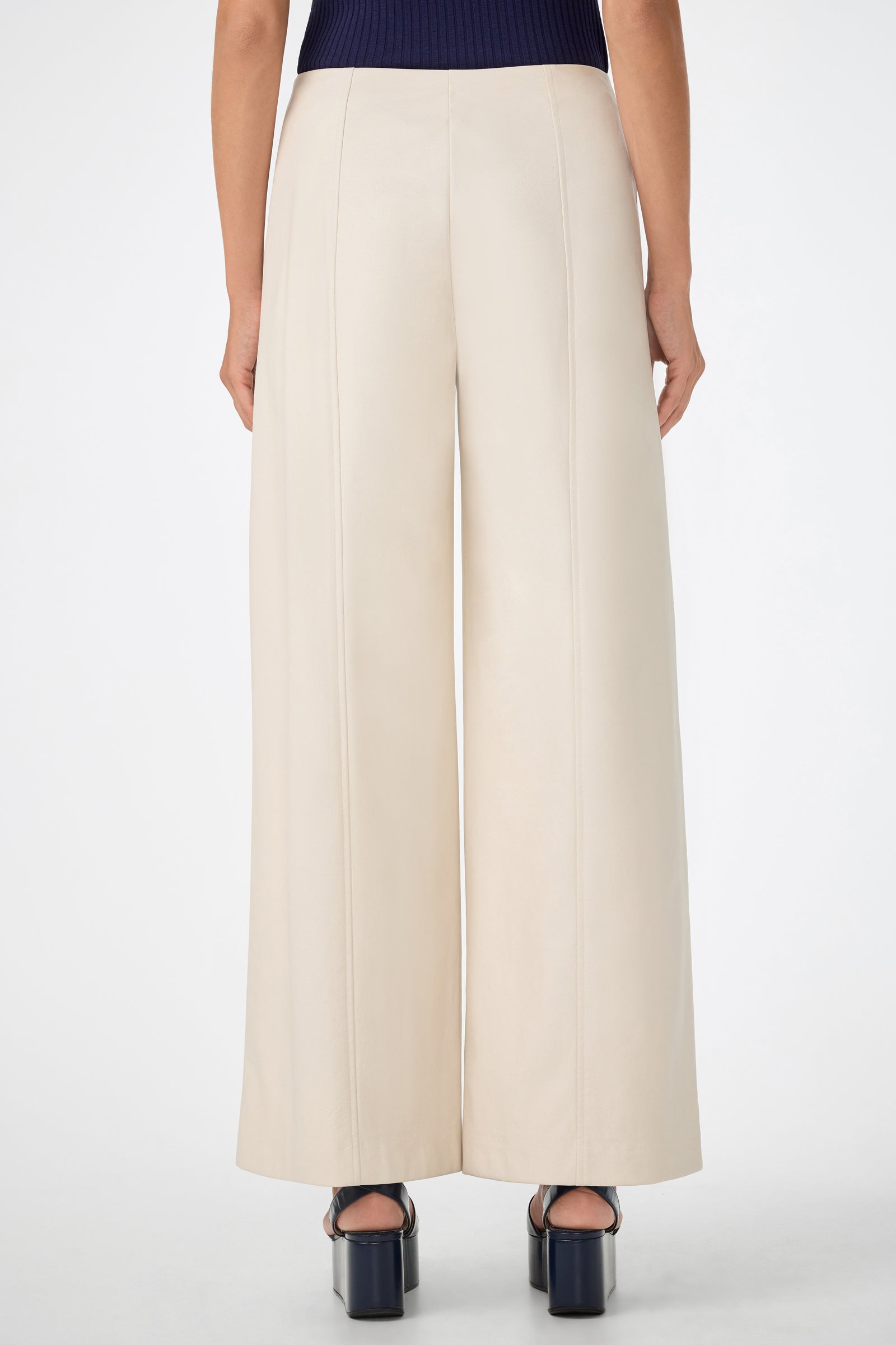 Someone wears the Parque Pant, a pair of high-waisted, wide-leg cream pants, with black platform heels, shown from the back against a plain white background.