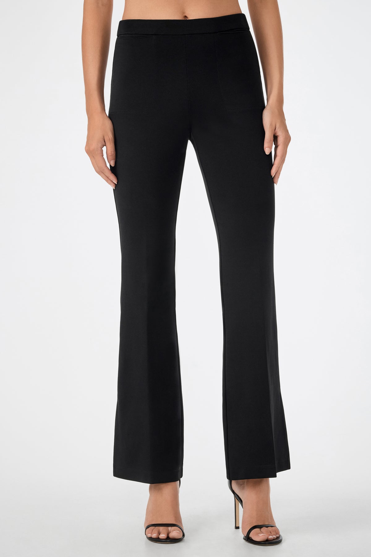A person wearing the Mona Pant—high-waisted, black, flared pants—and black high-heeled sandals, standing against a plain white background.