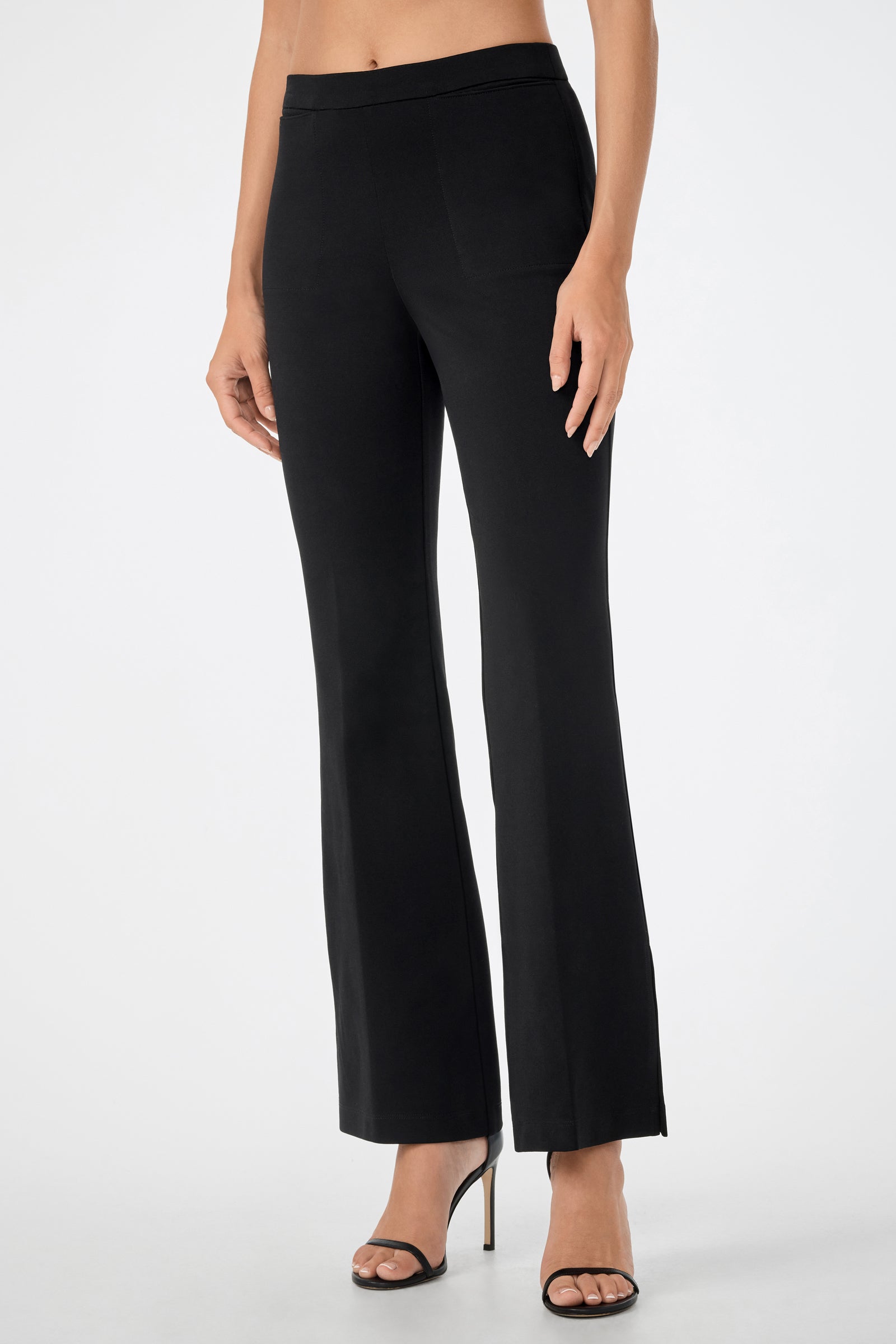 A woman models the Mona Pant—fitted black dress pants—with black high-heeled sandals, standing against a plain white background. Her upper body is mostly out of frame.