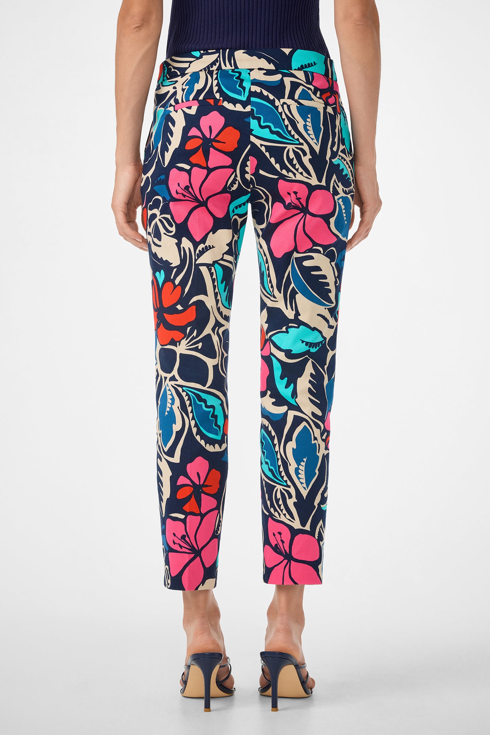 Person wearing the Moss 2 Pant—high-waisted, ankle-length pants with a vibrant floral pattern in blue, pink, red, and white—paired with heeled sandals and photographed from the back.