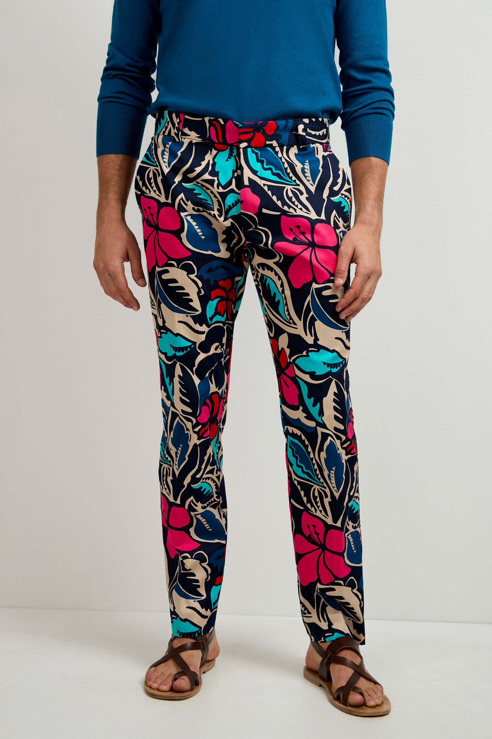 A person wearing a blue long-sleeve shirt, brown sandals, and the Clyde Slim Trouser - Copacabana with a colorful red, blue, and beige floral pattern, stands against a plain white background.