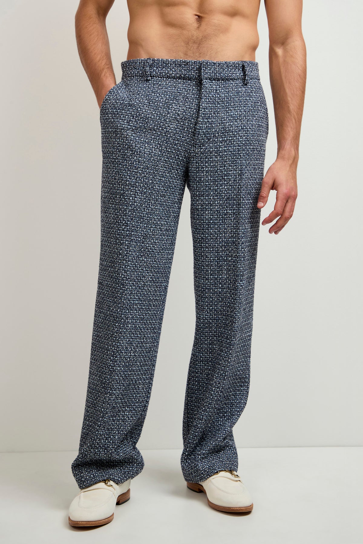 A shirtless man wearing Buckingham Tweed Trouser with hands in pockets stands against a plain light background, sporting white loafers.