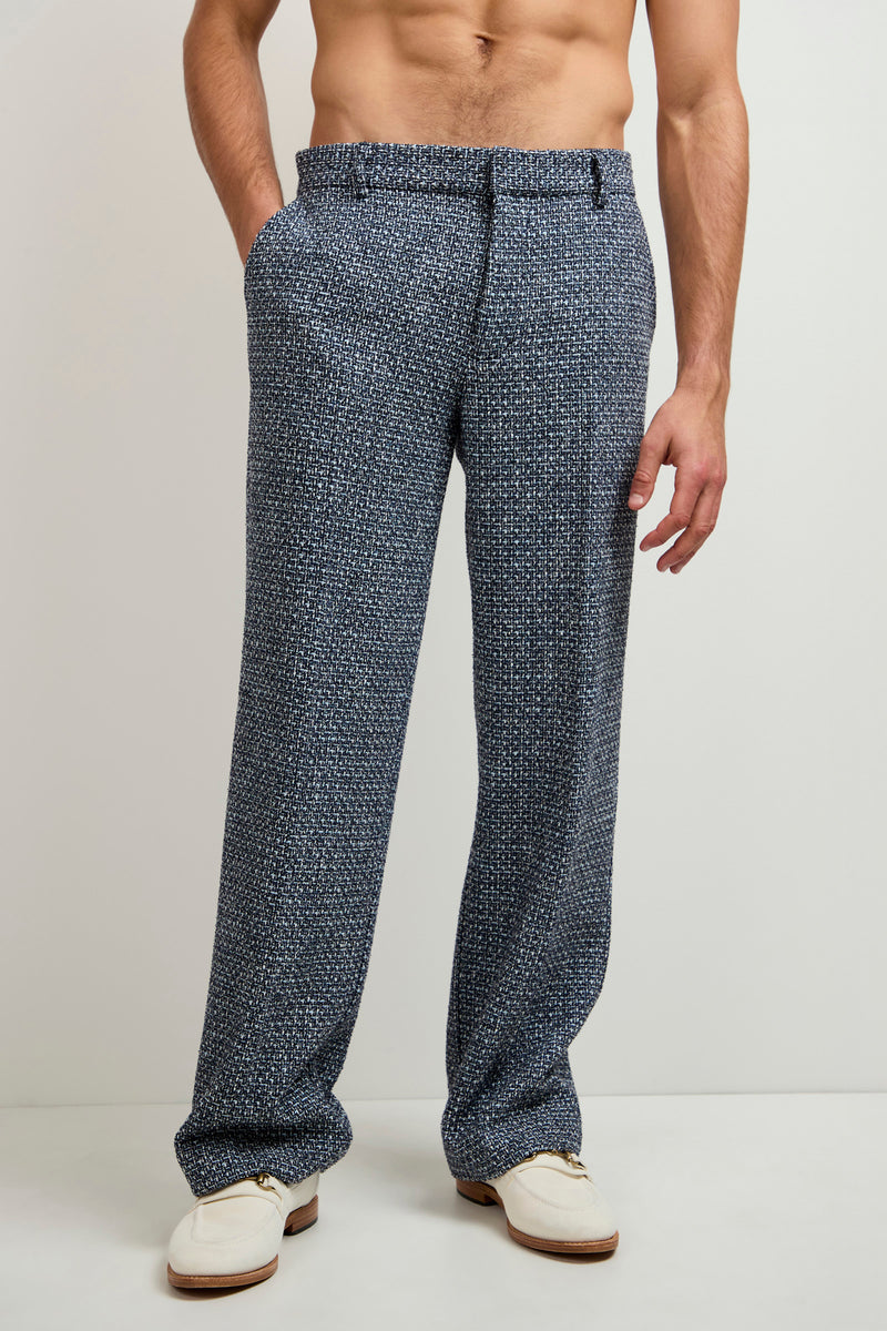 A shirtless man wearing Buckingham Tweed Trouser with hands in pockets stands against a plain light background, sporting white loafers.