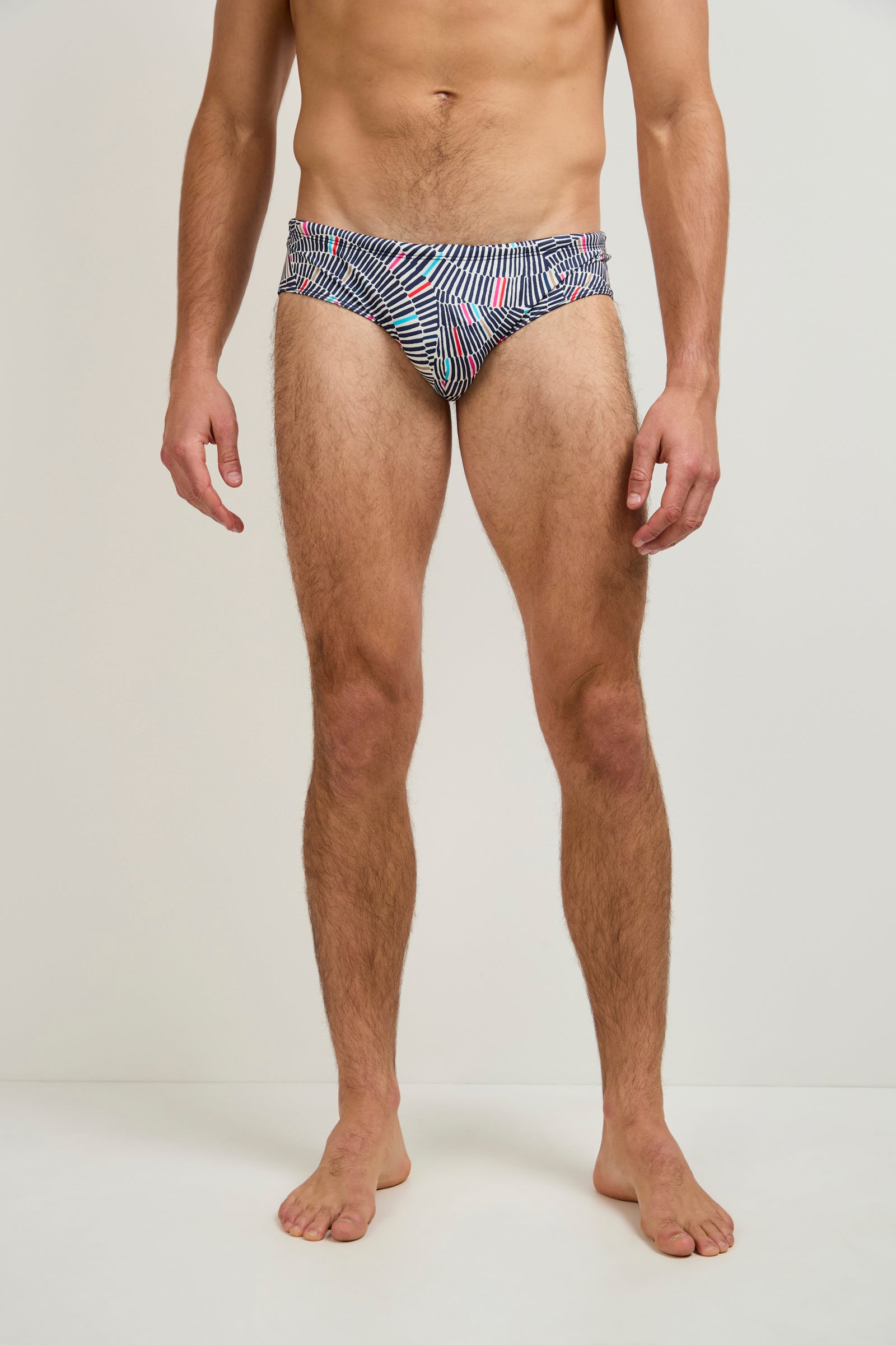 A man stands barefoot against a plain background, wearing Bondi Swim Trunk - Java, featuring a blue, white, and pink abstract pattern. His hands are at his sides and his face is not visible.