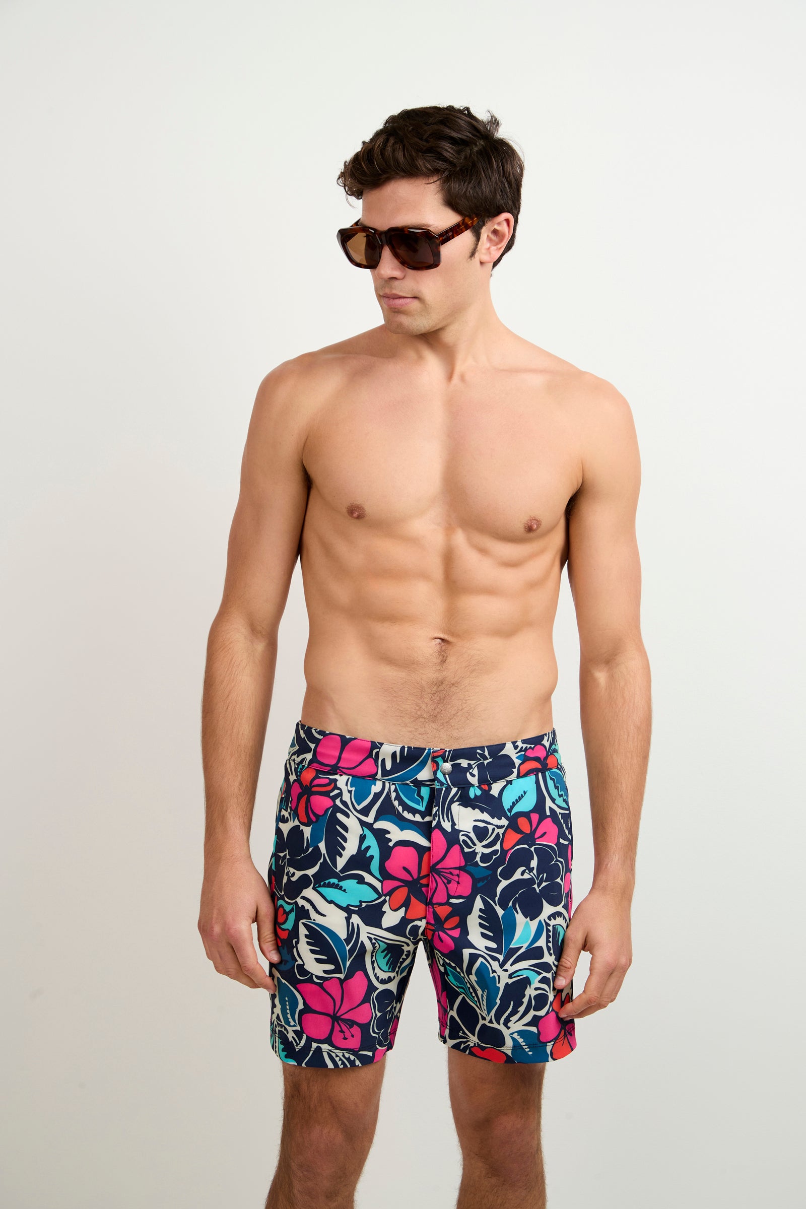 A shirtless man in dark sunglasses and Copacabana-colored Honolulu Board Shorts stands against a plain light background, looking slightly to his left.