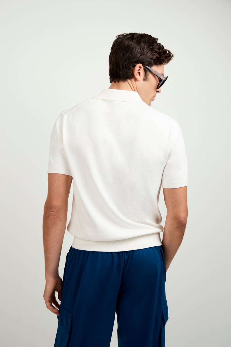 A man with short brown hair, in sunglasses and blue cargo pants, faces away from the camera wearing the Alvarez Short-Sleeve Polo against a plain light background.
