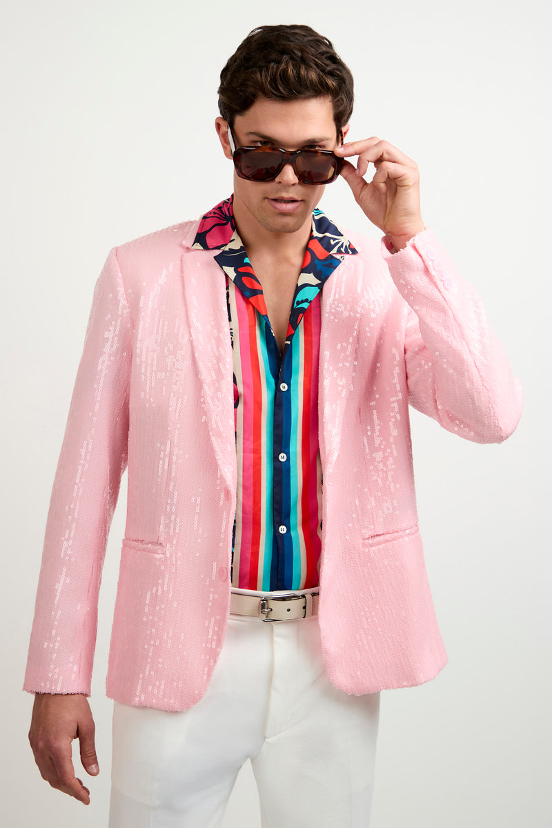 A man wearing the Bowie Sequin Blazer, a vibrant striped shirt, white pants, and sunglasses adjusts his shades while looking down against a plain white background.
