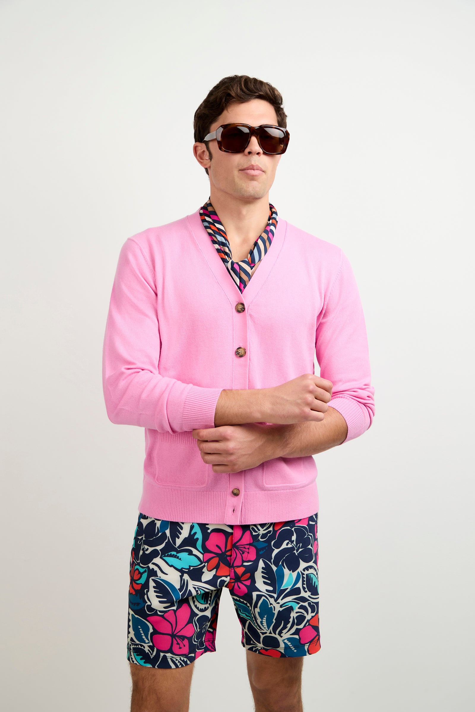 A man in sunglasses wears the Jacques Cardigan, featuring a colorful collar, paired with navy blue floral print shorts, standing against a plain white background.